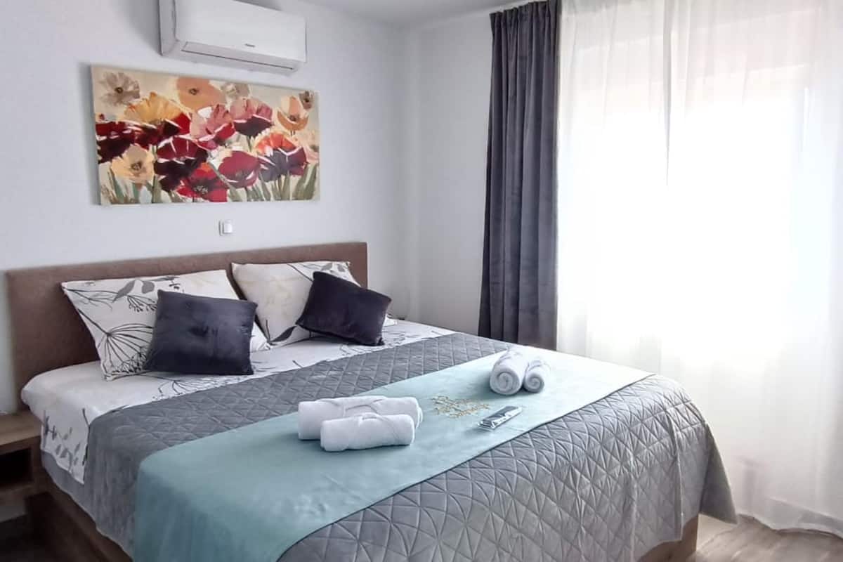 Un lit bien fait, avec une couverture matelassée, des oreillers et des serviettes enroulées, posés sur un plancher en bois.