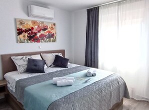 A neatly made bed with a quilted cover, pillows, and rolled towels on a wooden floor. - Dalmatia Apartments (Pakostane)