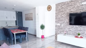 Un salon moderne comprenant un coin repas, un téléviseur à écran plat fixé à un mur à l’aspect pierre, et un aménagement de style minimaliste.