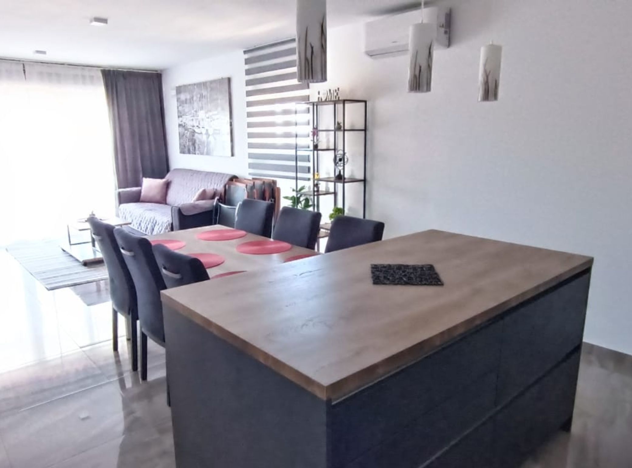 A modern living room with a wooden dining table, black chairs, and a sofa with a grey throw.