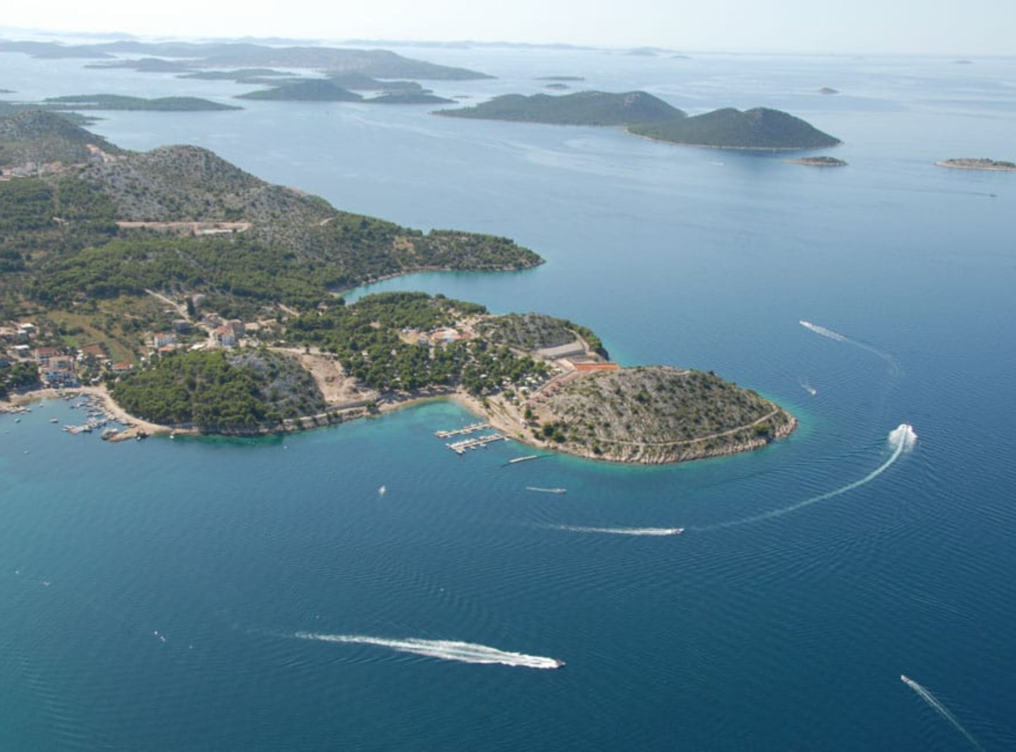 Vue aérienne d’une zone côtière comprenant de nombreuses îles, des eaux d’un bleu limpide et un petit village avec des bâtiments et des quais.