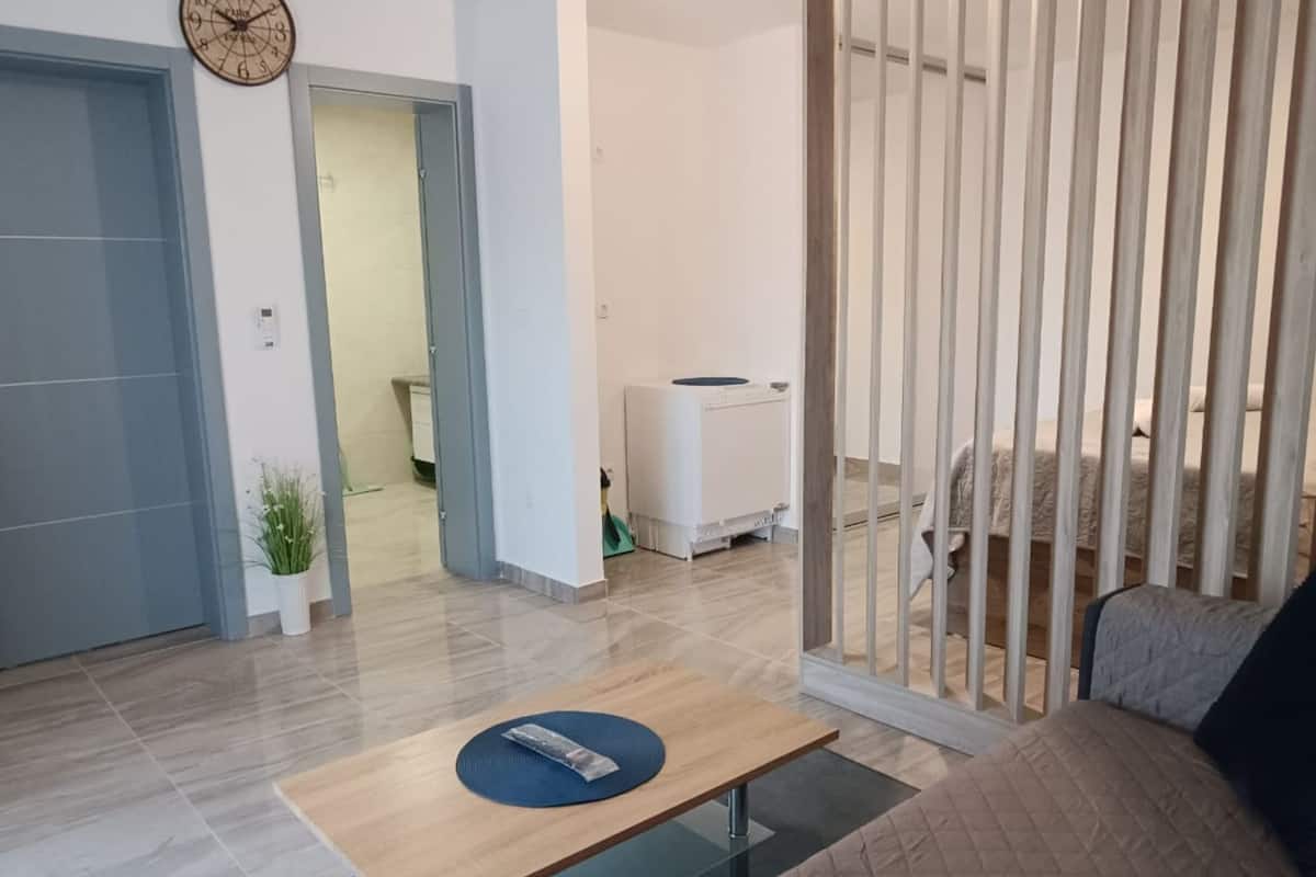 Un salon moderne avec un canapé, une table basse et un téléviseur. Une porte donne accès à une autre pièce et une plante est placée dans un coin.