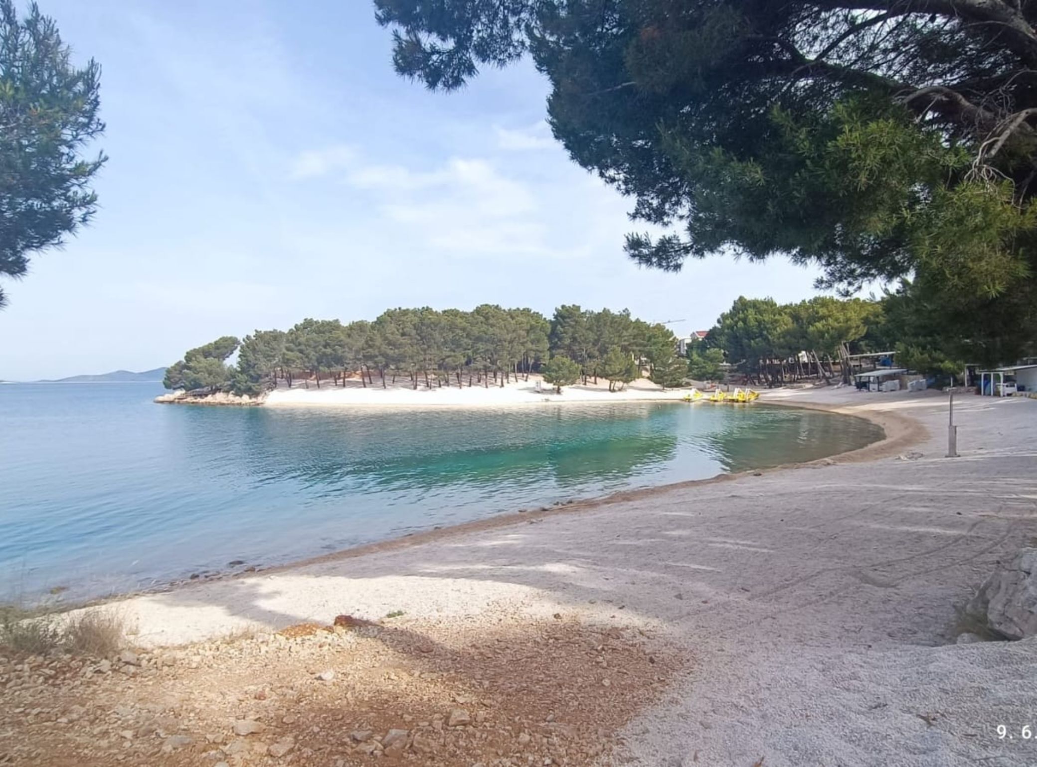 A beach with a sandy shore, a small island with trees, and a clear blue sea.