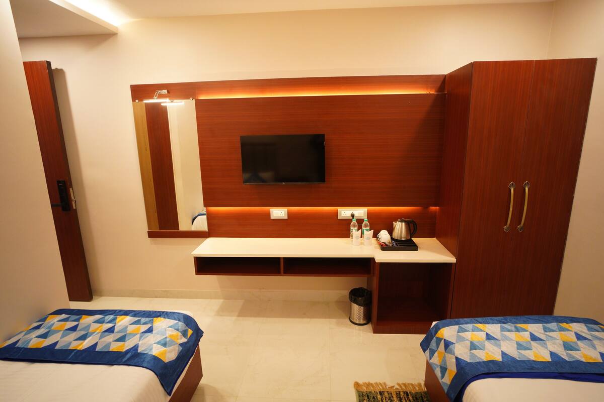 Habitació d'hotel amb dos llits, un televisor fixat a la paret, un armari de fusta i una taula petita amb mirall i articles de tocador.