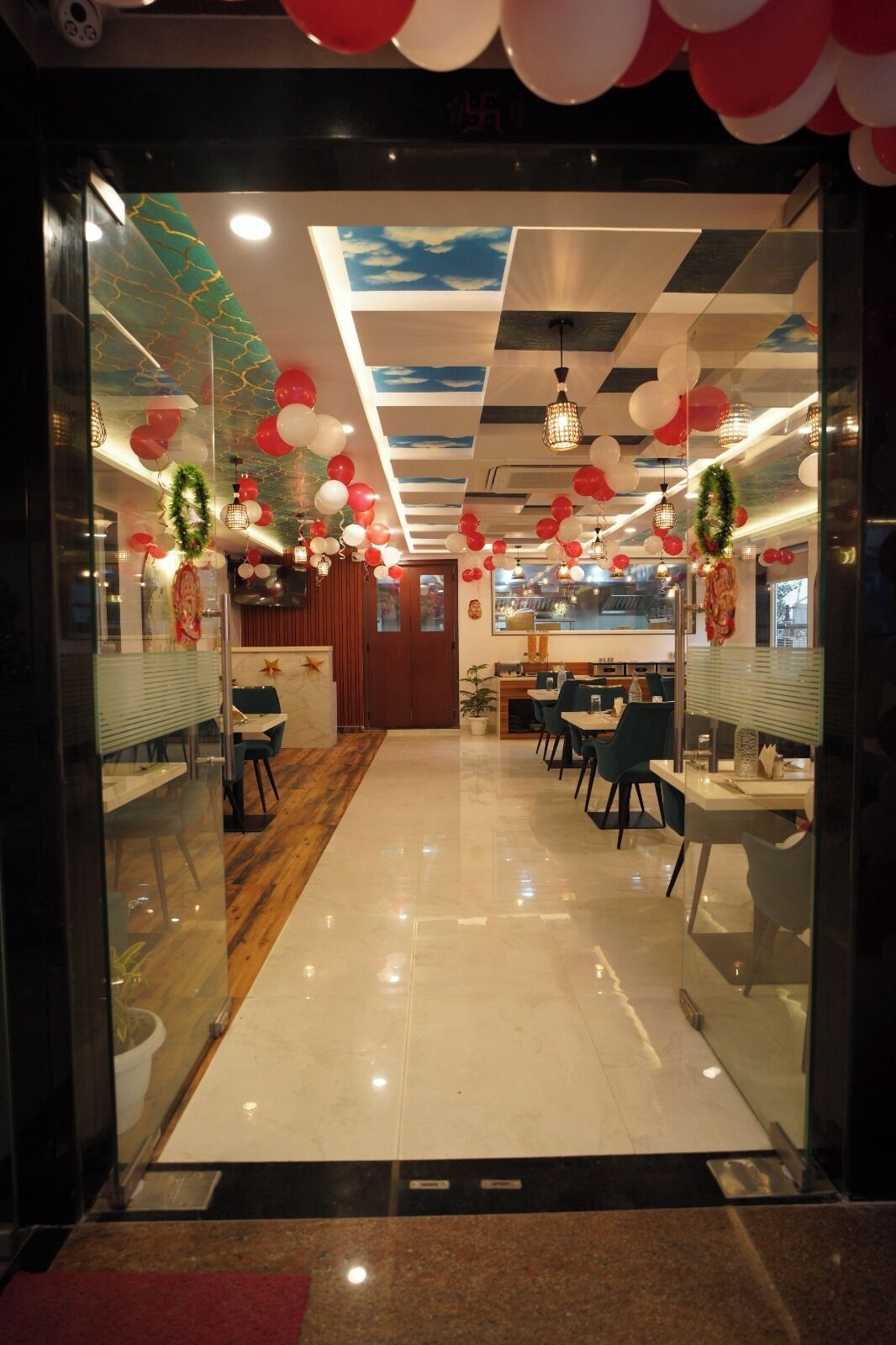A restaurant with a modern interior, featuring a glass entrance, a wooden reception desk, and a seating area with tables and chairs.