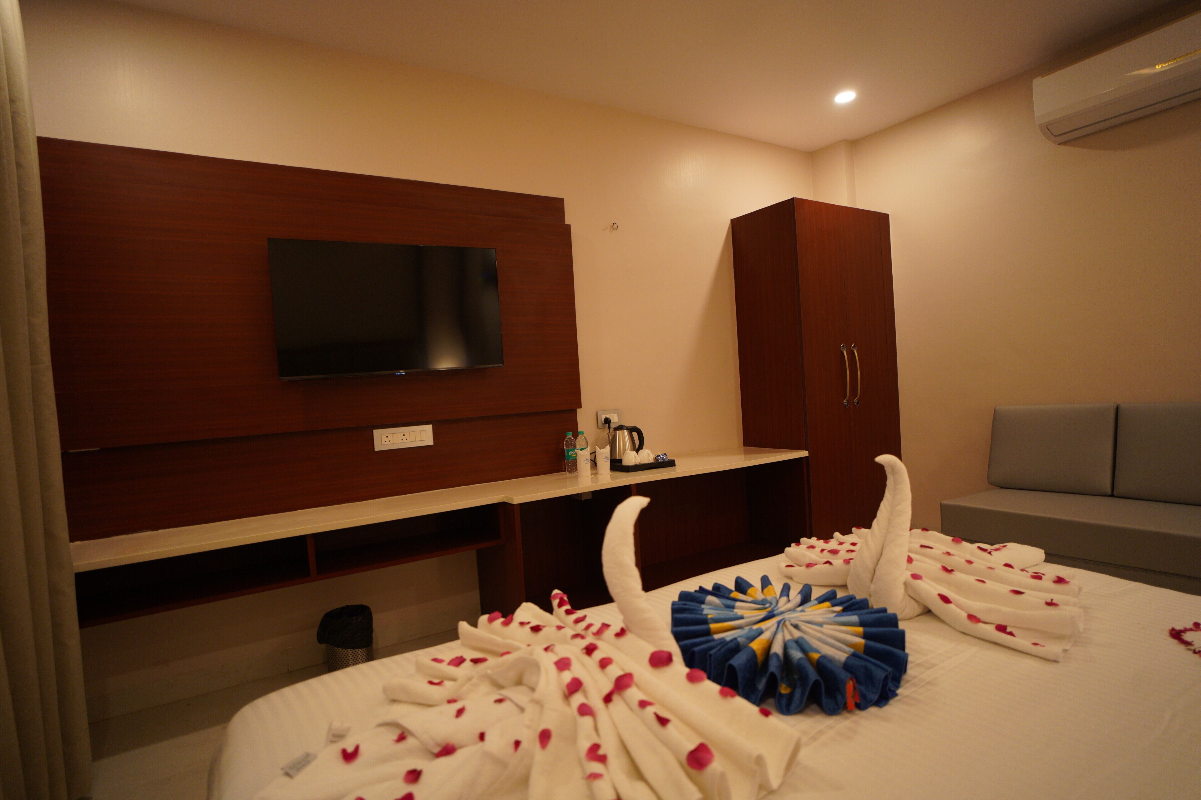 A hotel room with a bed, a TV mounted on the wall, a wardrobe, and a sofa.