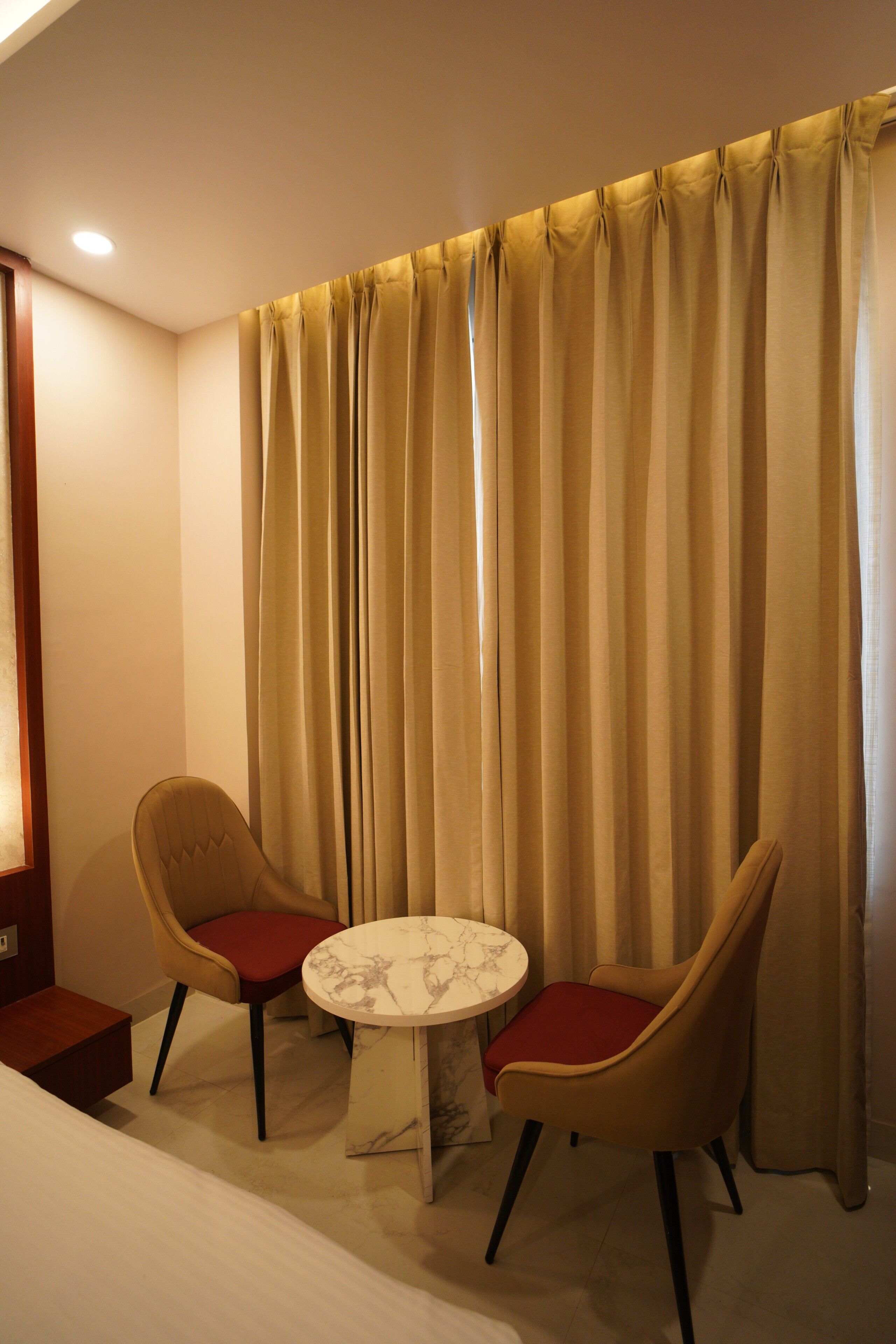 A hotel room with a bed, a round table, two chairs, and a curtain.