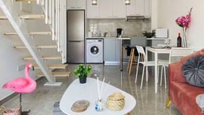 A modern apartment with a kitchen, dining area, and living room. It includes a staircase, a washing machine, a dining table with chairs, and a sofa. - Pink Flamingo 1-BR Apartment in Larnaca (Larnaca)