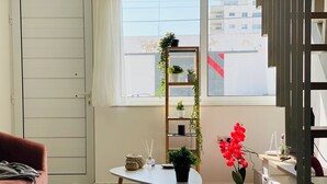 A modern living room with a pink sofa, a white table, and a plant shelf by the window. - Pink Flamingo 1-BR Apartment in Larnaca (Larnaca)