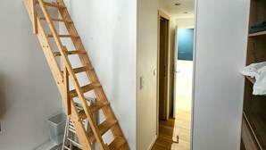 A room with a wooden ladder against the wall, a white door, and a hallway leading to another room. - Big flat - Le Cala - City Center (Nice)