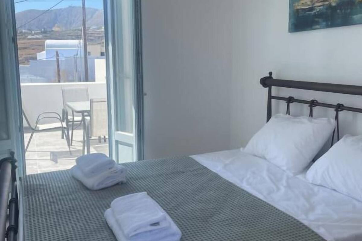 Una habitación de hotel con una cama, un cuadro en la pared y vistas a través de una puerta abierta.