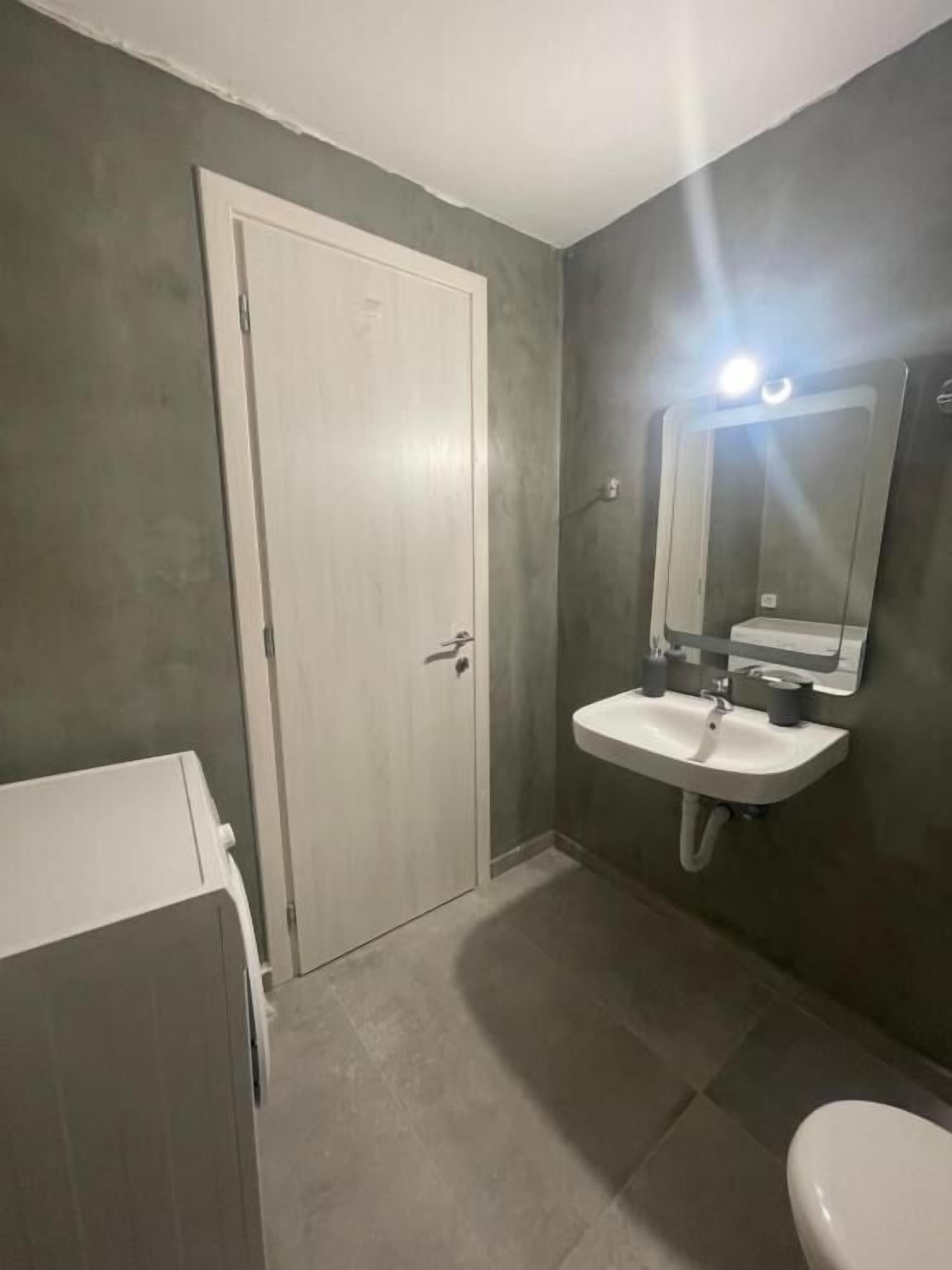 Ein Badezimmer mit weißer Tür, Waschbecken mit Spiegel und Toilette.