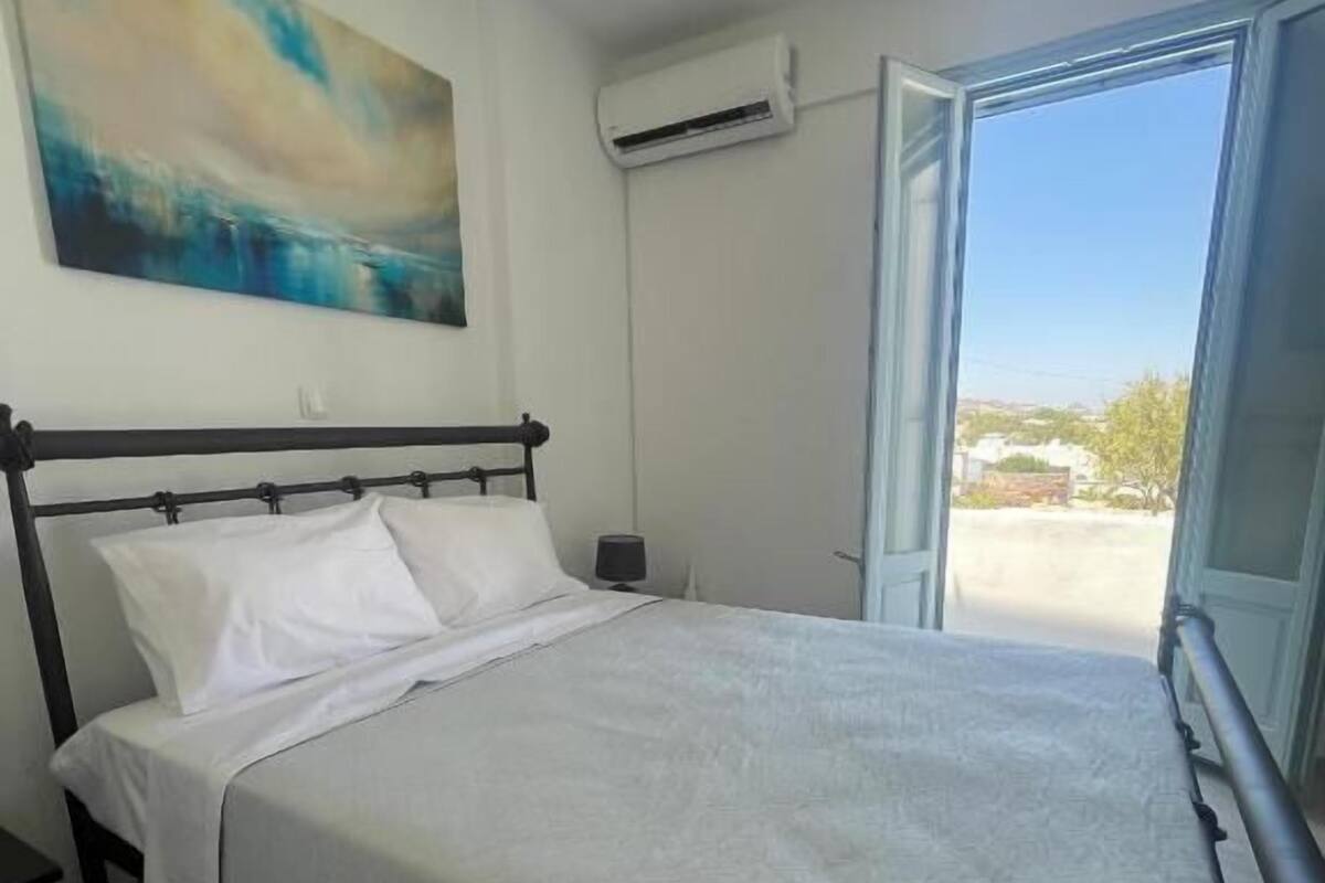Un dormitorio con una cama, una mesita de noche, un equipo de aire acondicionado y una ventana con vistas al exterior.