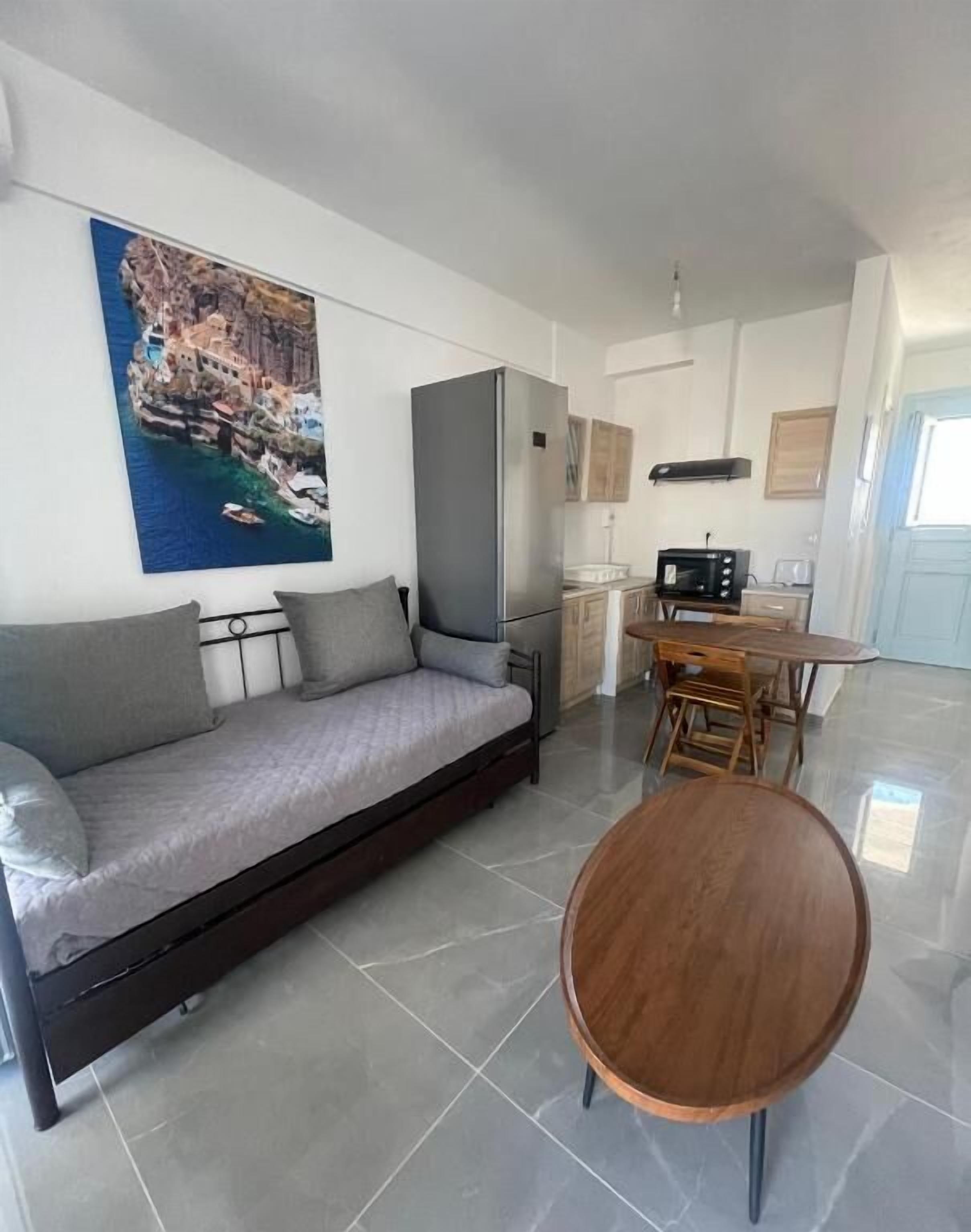 A modern living room with a sofa, a wooden coffee table, and a kitchen area with a refrigerator and microwave.