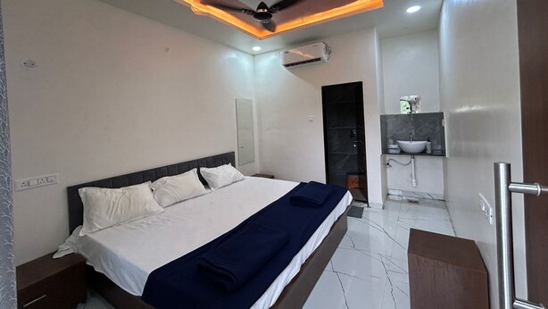 A modern hotel room with a large bed, a ceiling fan, an air conditioning unit, and a bathroom with a sink and mirror. - MORESHWAR PRIDE & RESIDENCY (Khuldabad)