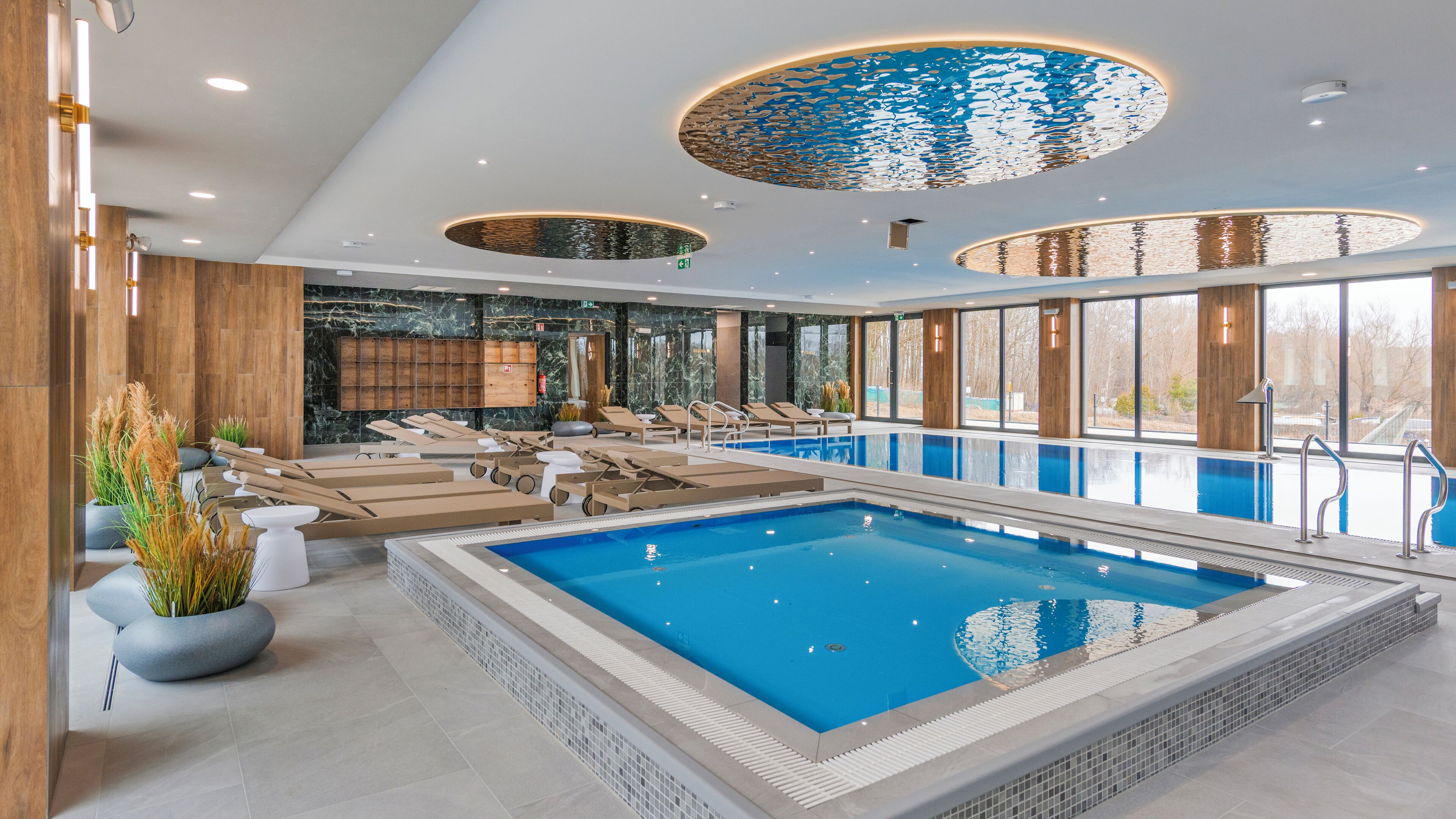 Una piscina interior moderna con sillones de descanso y vistas al exterior.