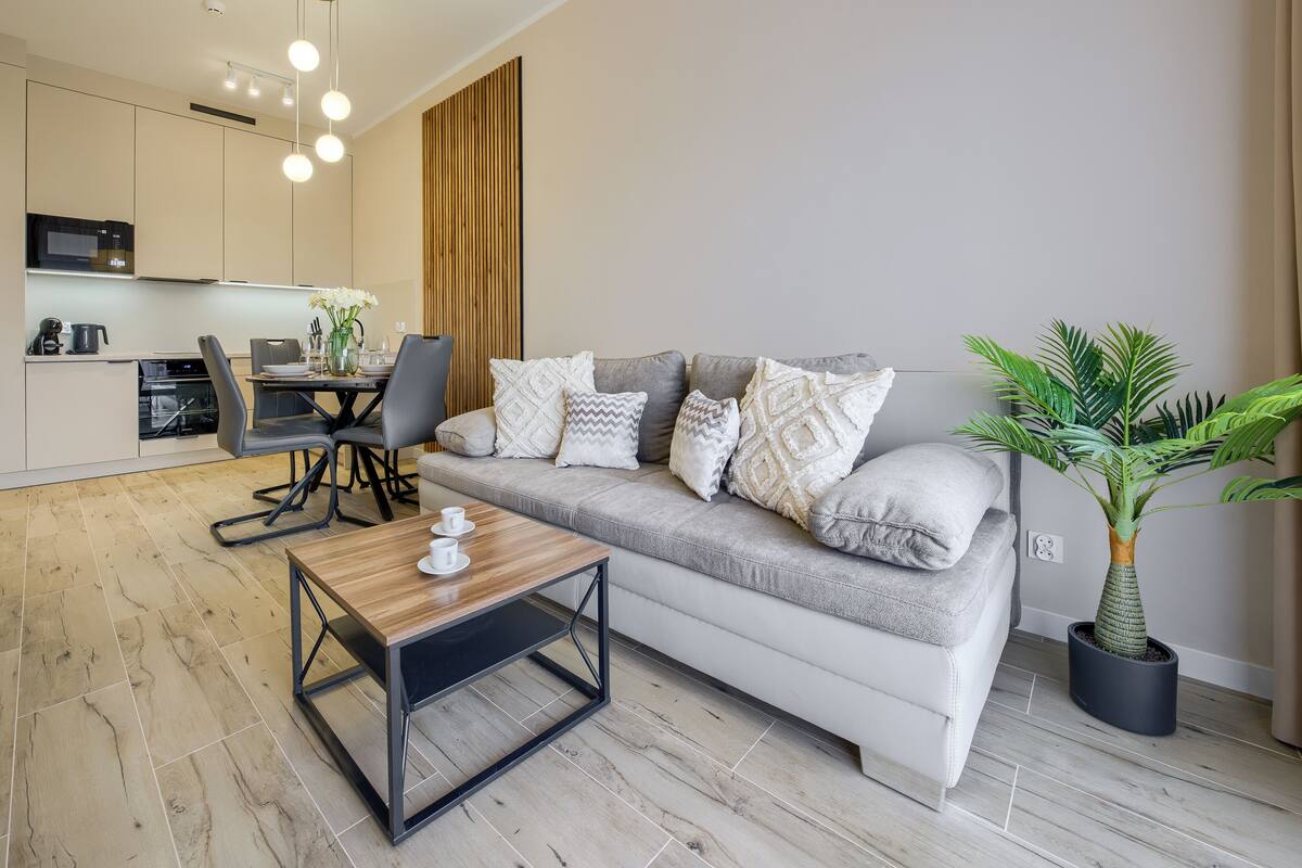 Ein modernes Wohnzimmer mit einem grauen Sofa, einem Holztisch und einem Essbereich inklusive Tisch und Stühlen.