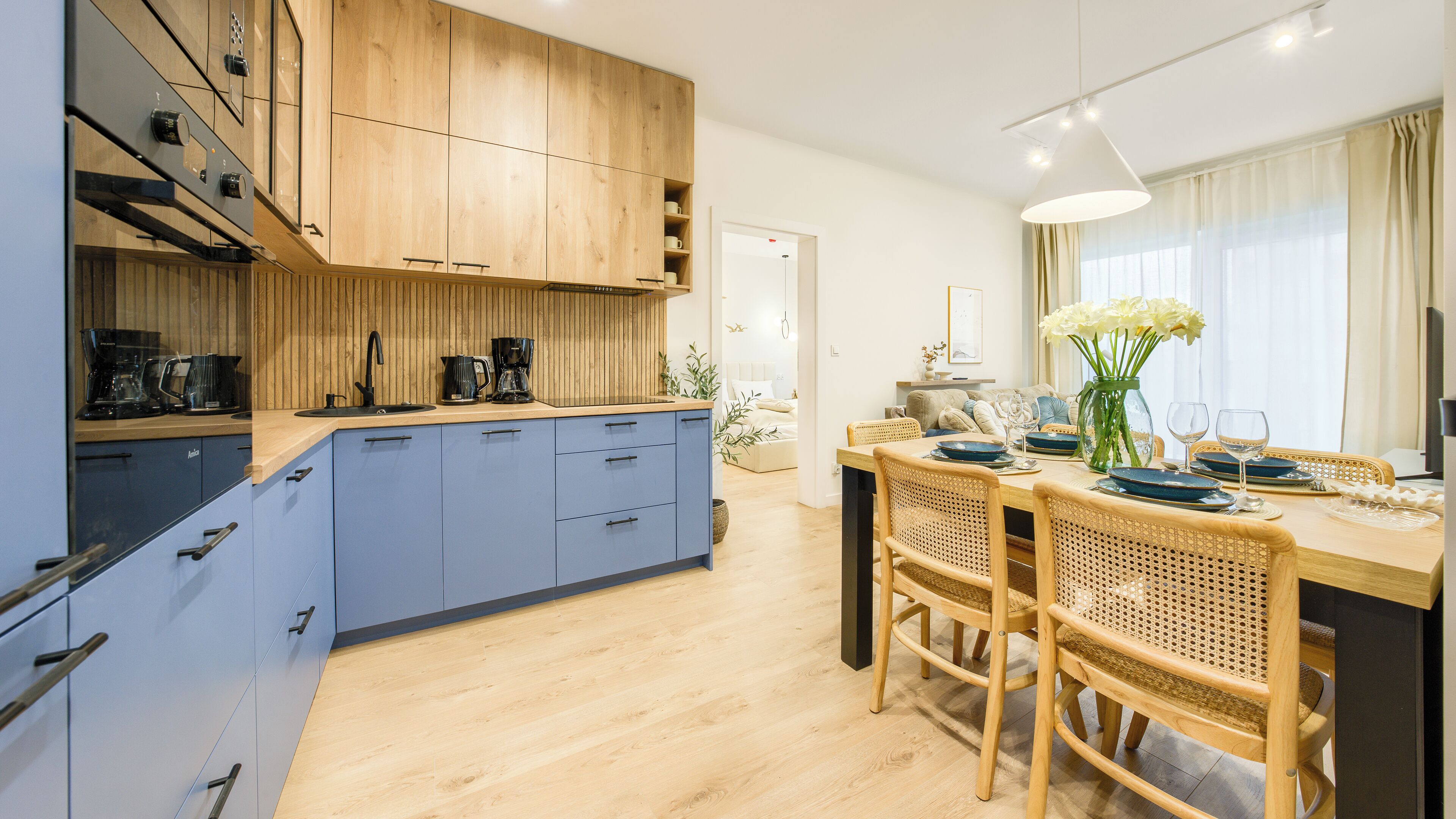 A modern kitchen with blue cabinets, wooden countertops, and a dining area with a wooden table and chairs.