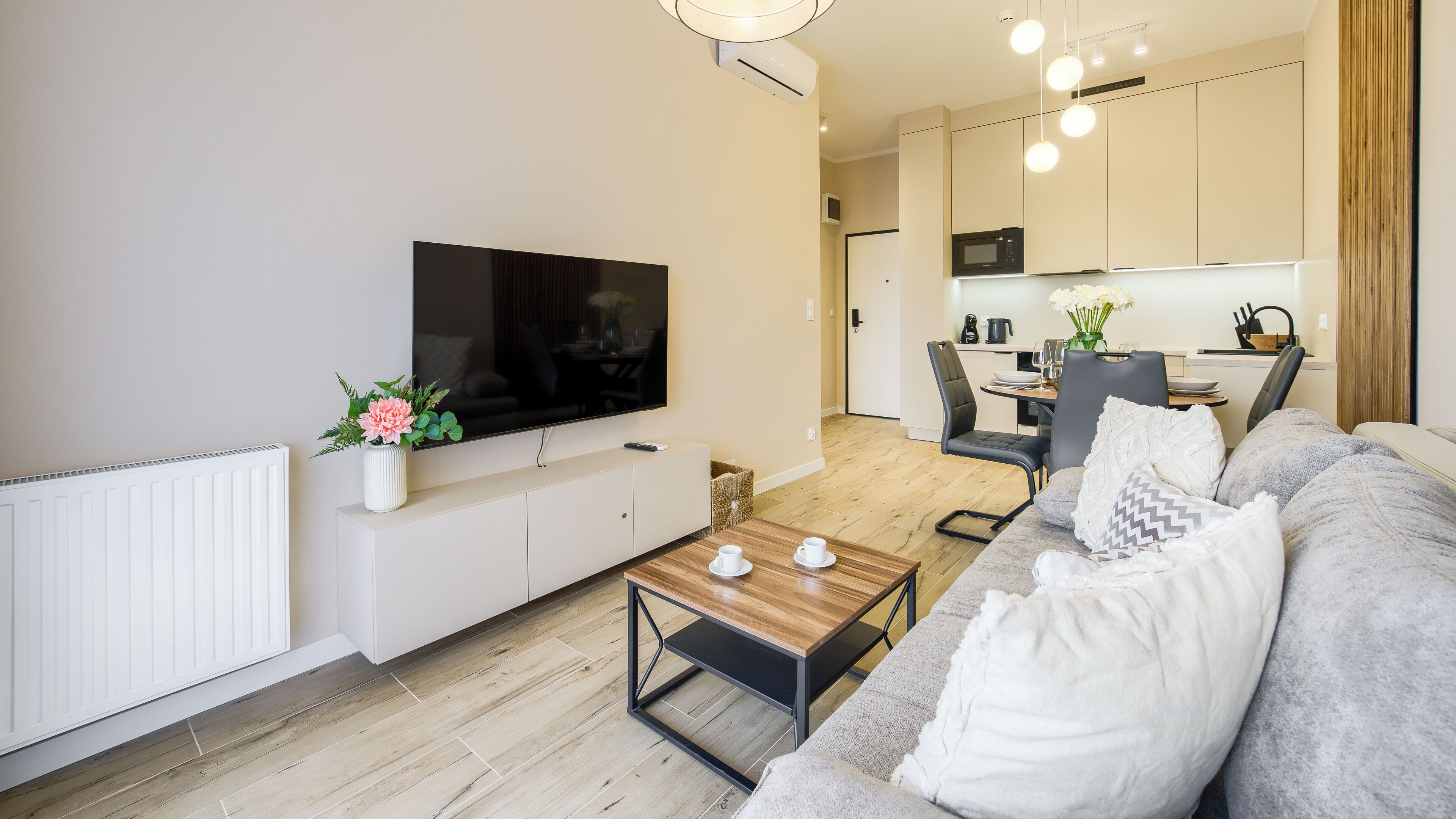 A modern living room with a flat-screen TV, sofa, coffee table, and a dining area with chairs and a table.