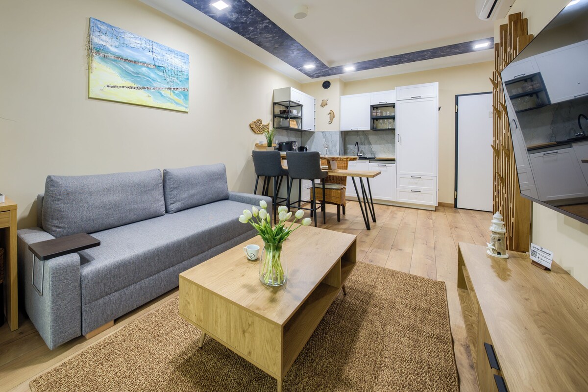 Ein modernes Wohnzimmer mit einem grauen Sofa, einem Holztisch und einem Essbereich mit kleinem Tisch und Stühlen.