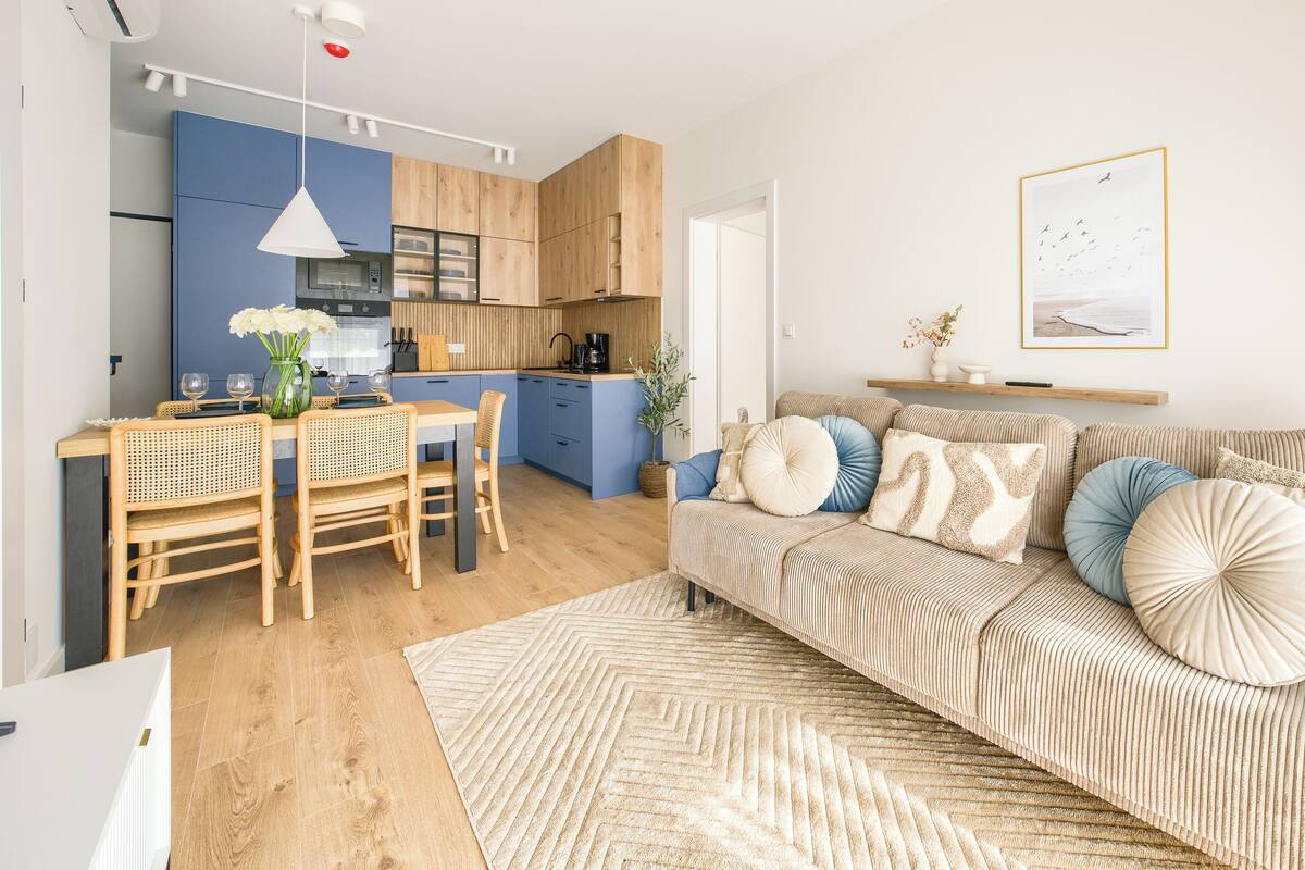 Eine moderne Küche mit Holzausstattung, ein Essbereich mit Tisch und Stühlen sowie ein Wohnzimmer mit Sofa und Kissen.