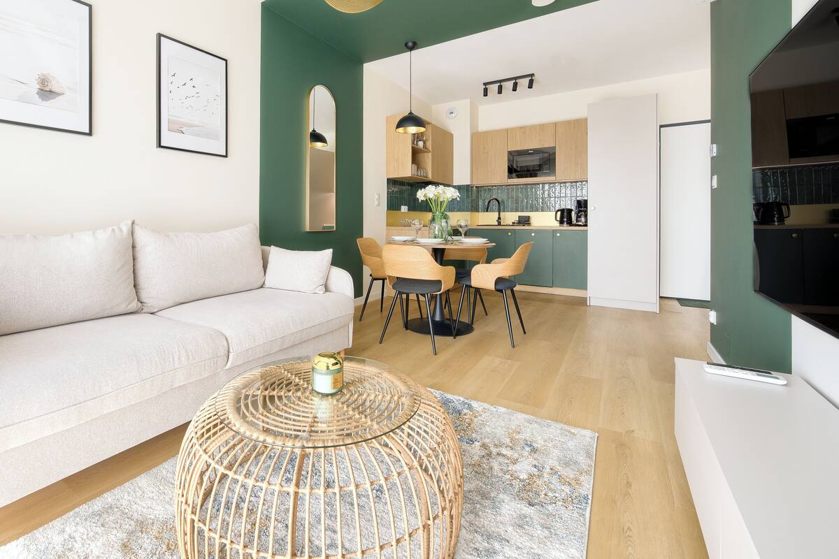 Ein modernes Wohnzimmer mit einer Couch, einem Esstisch, Stühlen und einer Küche im Hintergrund.