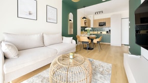A modern living room with a sofa, dining table, chairs, and a kitchen in the background. - Apartamenty Sun & Snow The One Ustronie Morskie (Sianożęty)