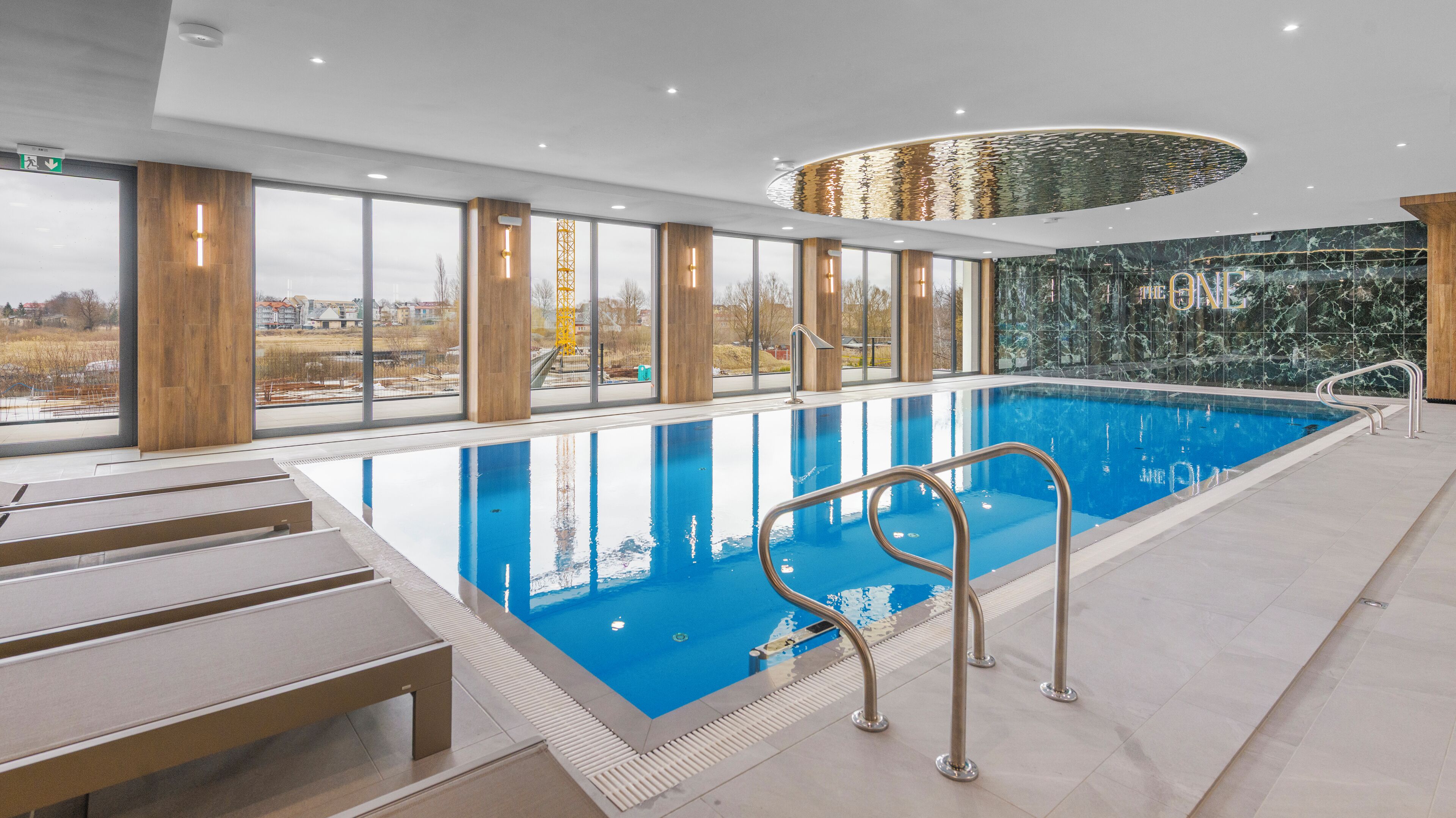 A modern indoor swimming pool with clear views of the outside, wooden pillars, and a marble wall.