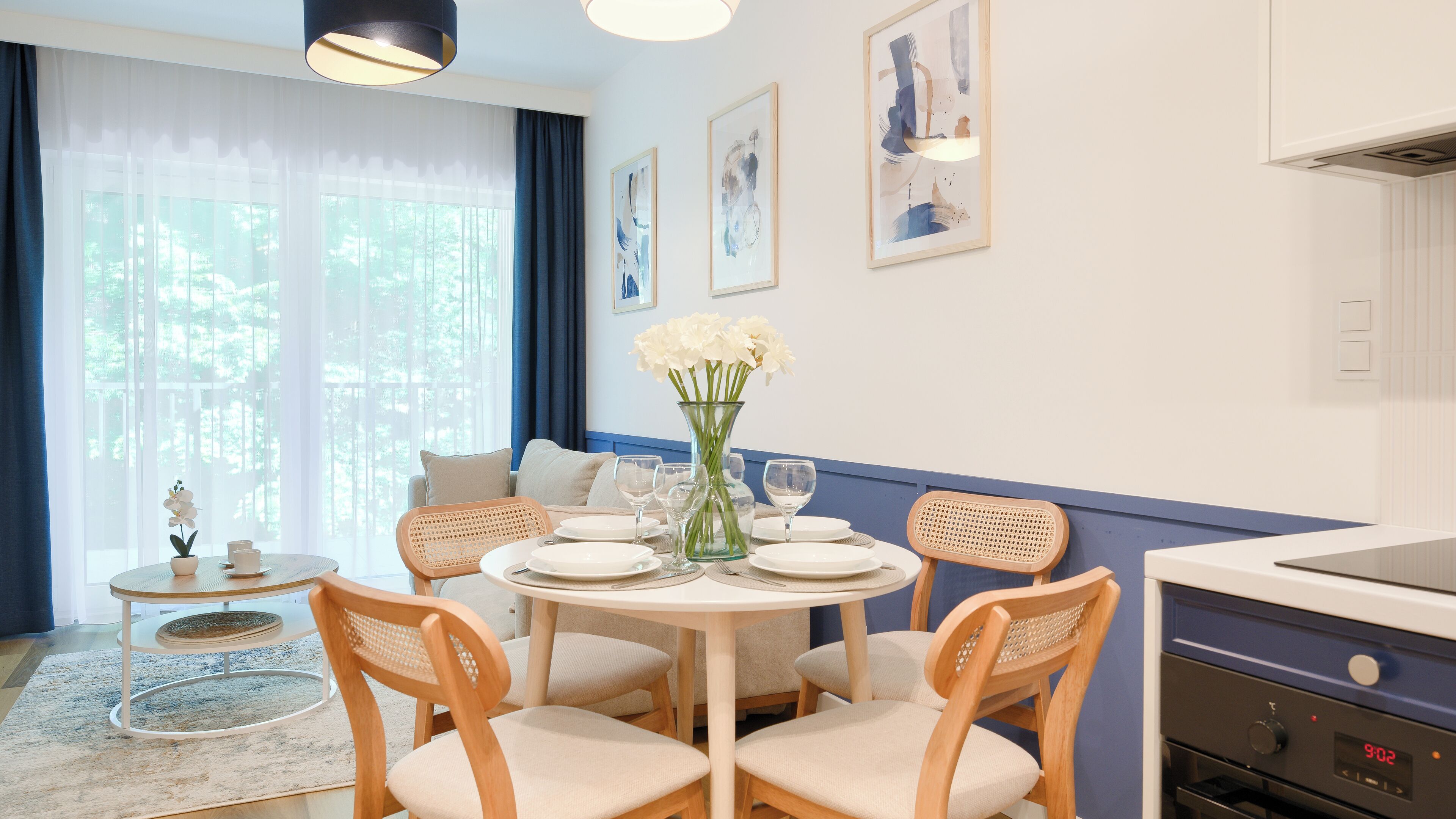 Comedor con una mesa redonda, sillas, un jarrón con flores y una zona de cocina con estufa.