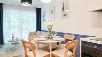 Comedor con una mesa redonda, sillas, un jarrón con flores y una zona de cocina con estufa.