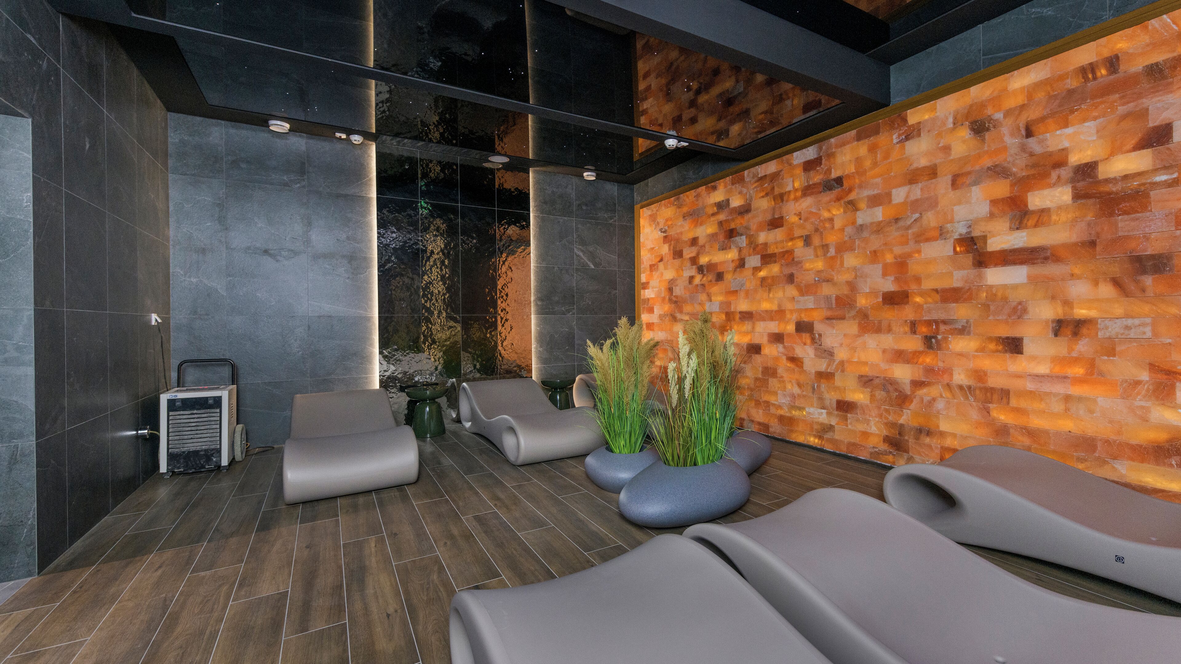 Un moderno espacio de spa con pared de piedra, sillones reclinables y camilla de masaje.