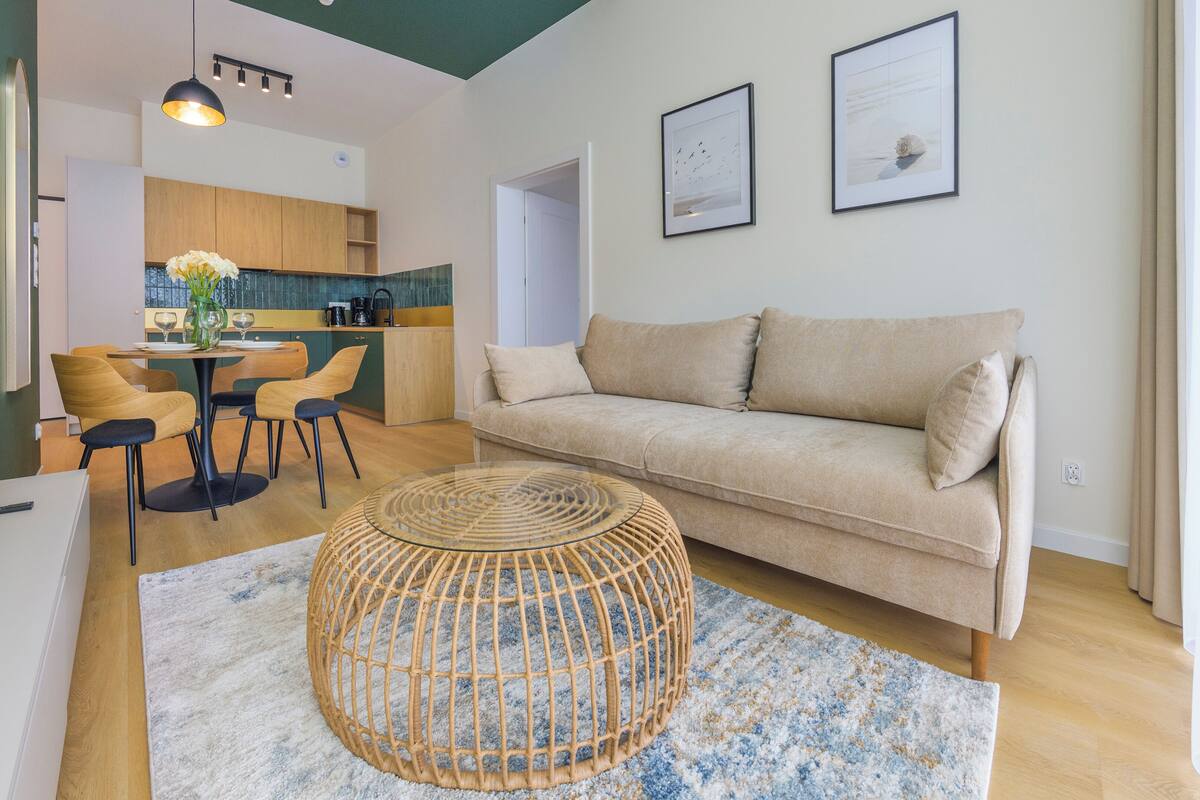Ein modernes Wohnzimmer mit einer Couch, einem Esstisch mit Stühlen, einer Küche im Hintergrund und zwei gerahmten Bildern an der Wand.