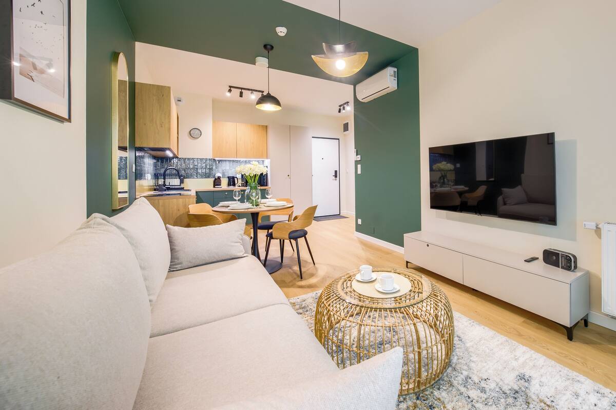 Ein modernes Wohnzimmer mit einer Couch, einem Esstisch mit Stühlen, einem Fernseher und einer Küchenzeile im Hintergrund.
