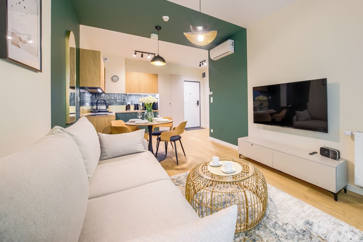 Una sala de estar moderna con un sofá, una mesa de comedor con sillas, un televisor y una cocina al fondo.