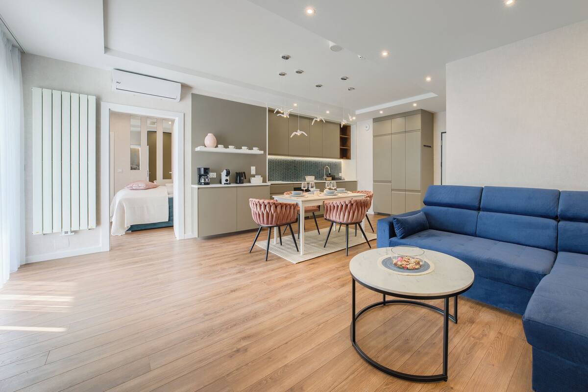 Ein modernes Wohnzimmer mit einem blauen Sofa, einem runden Couchtisch und einem Essbereich mit rosafarbenen Stühlen.