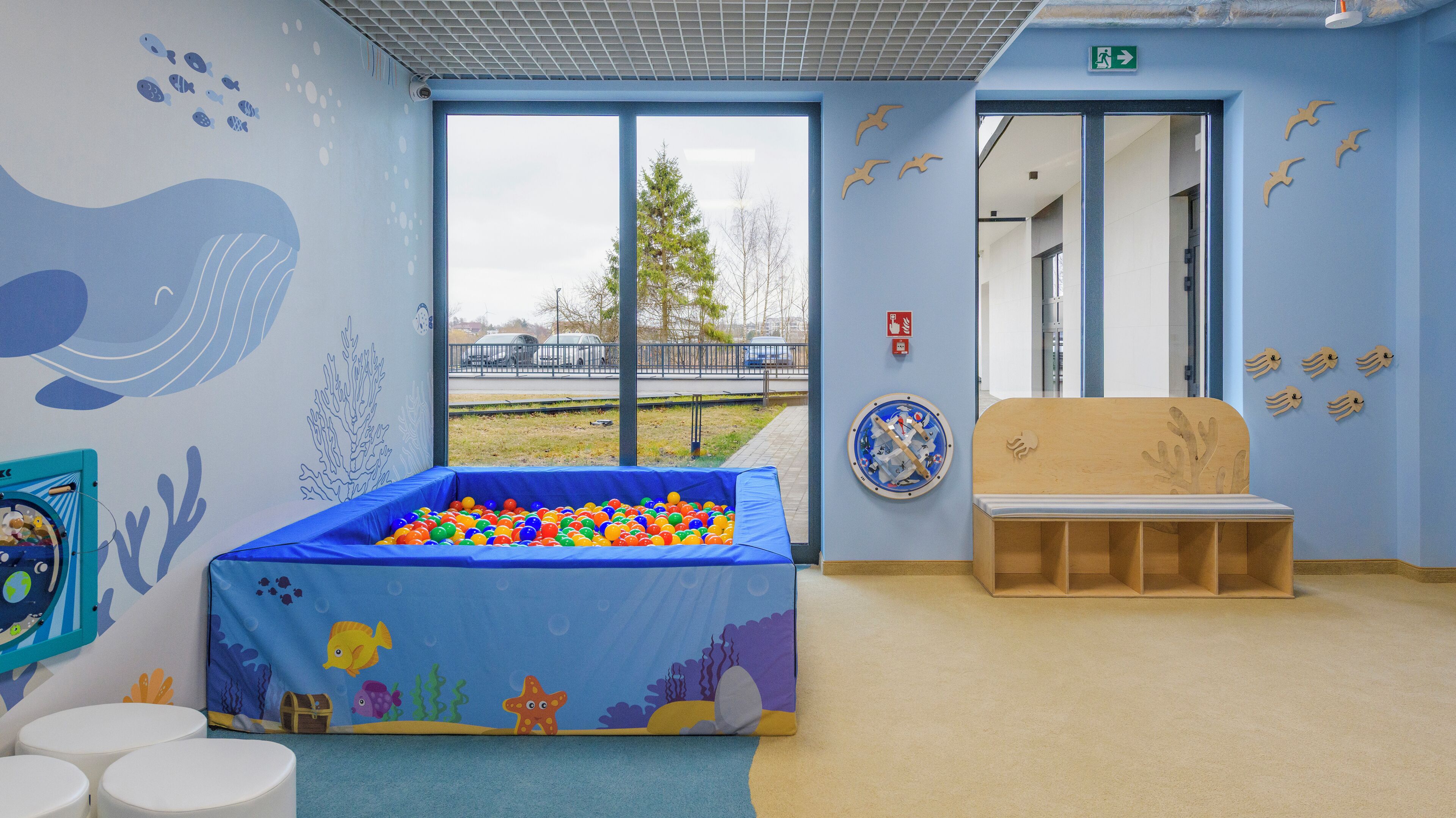 A children's play area with a ball pit, a wooden bench, and a mural with sea creatures.