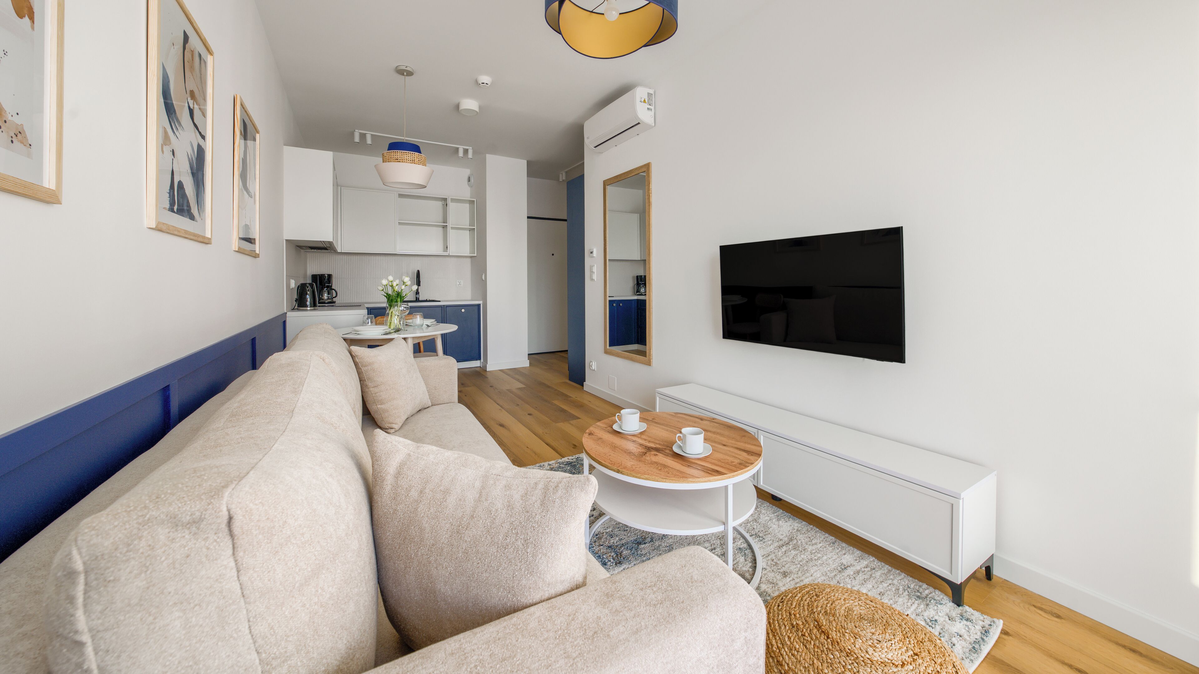 Un salon moderne avec un canapé d’angle, une table basse et un téléviseur à écran plat fixé au mur.