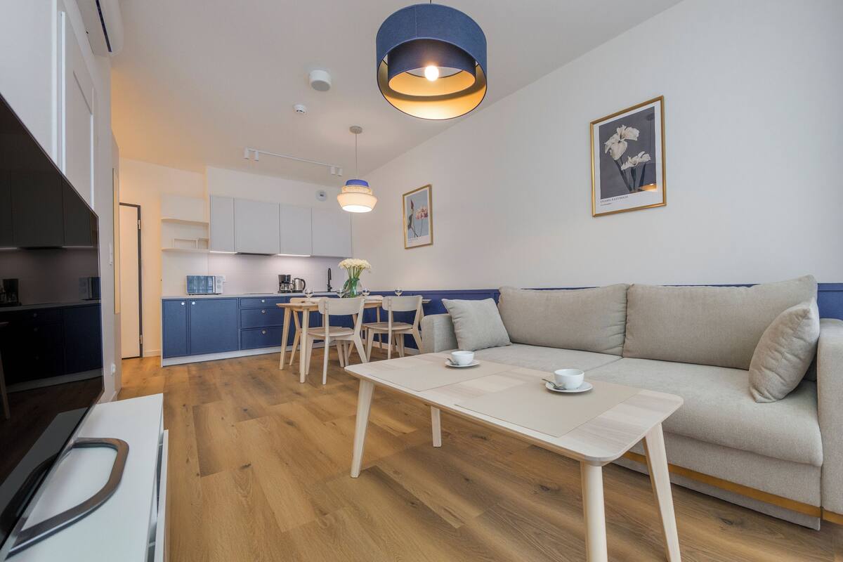 Ein modernes Wohnzimmer mit Sofa, einem Esstisch und einer dahinterliegenden Küche.