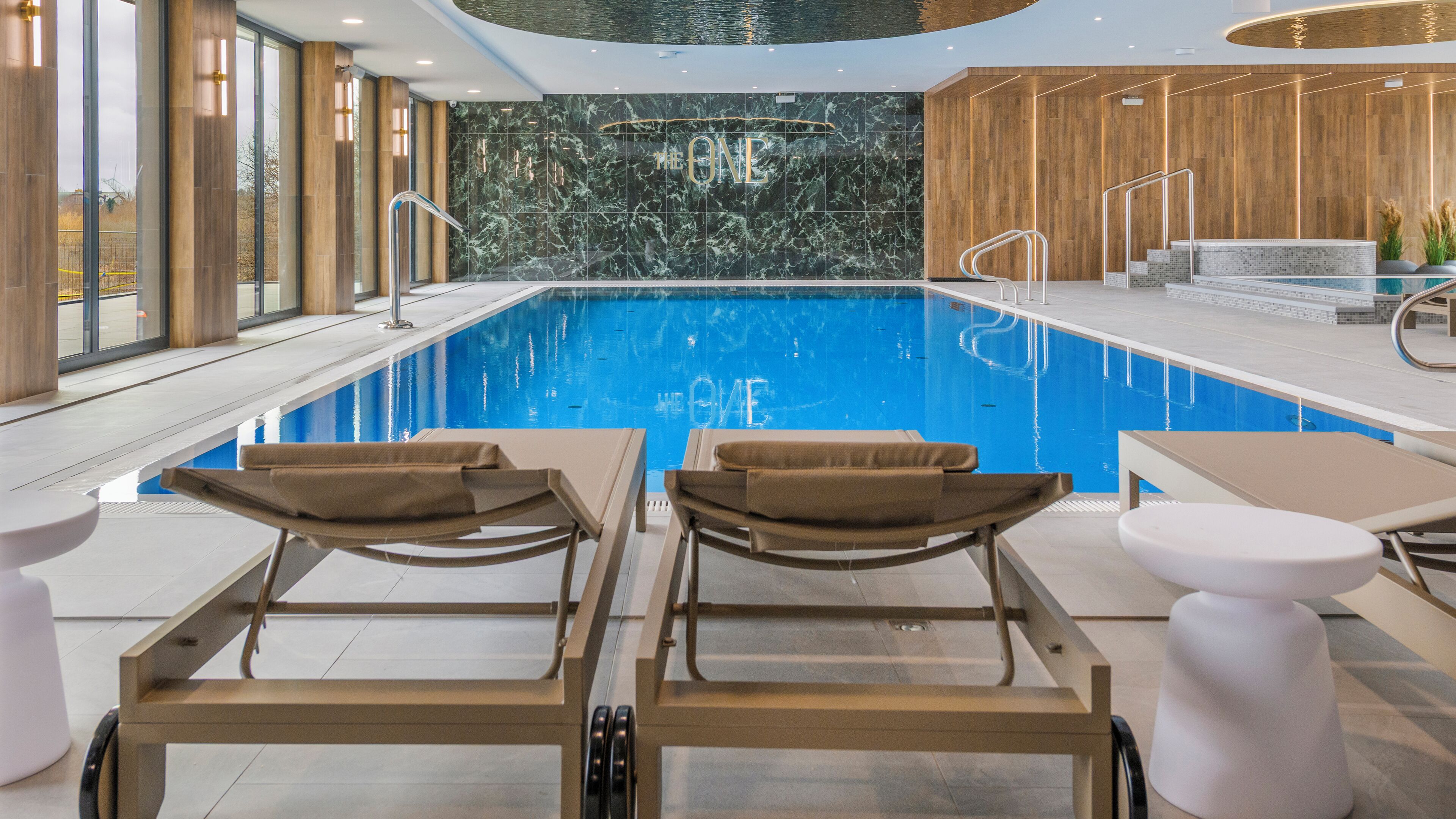 An indoor swimming pool with lounge chairs and a wooden wall with 'THE ONE' written on it.