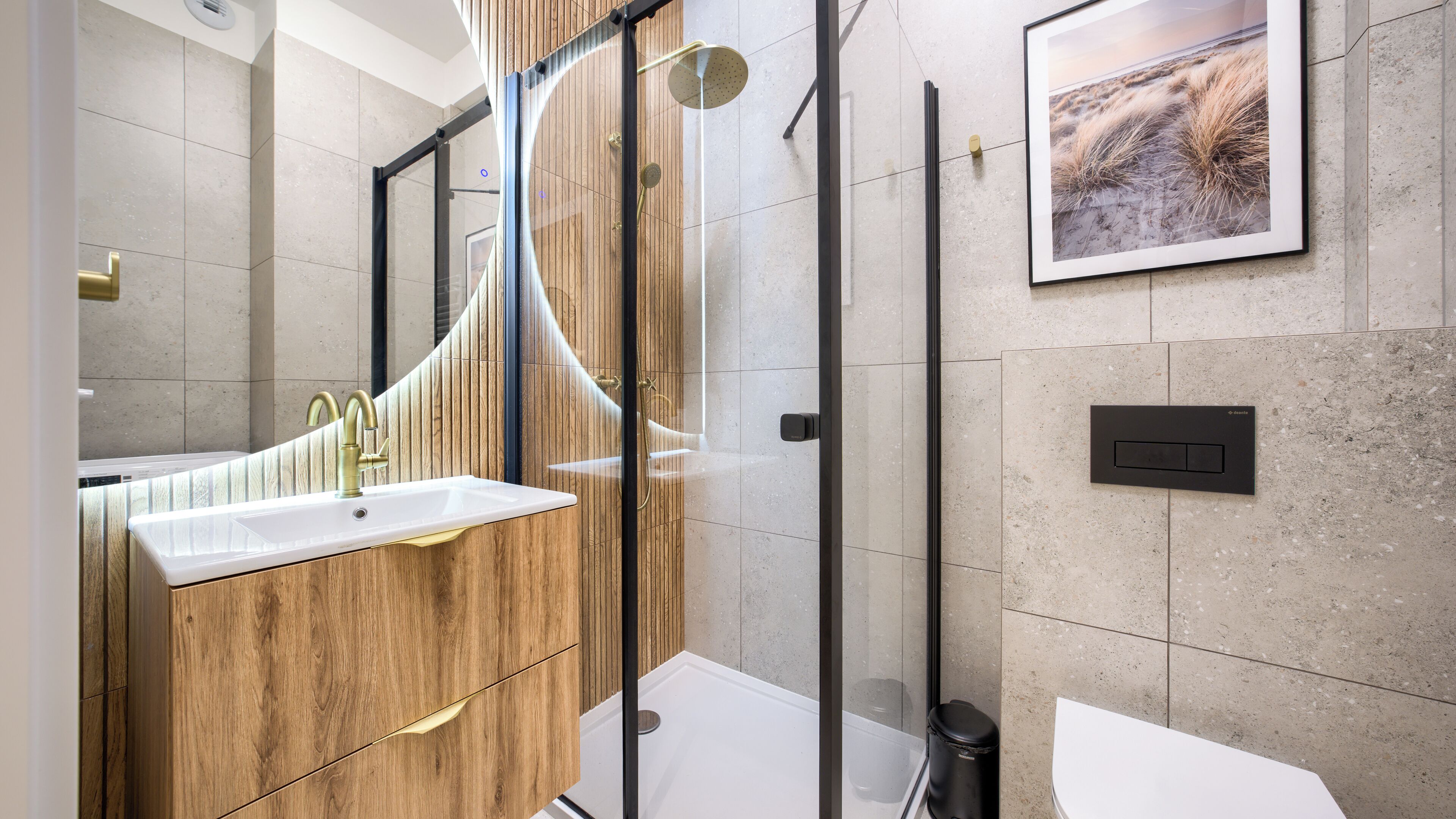 A modern bathroom with a wooden vanity, a glass shower enclosure, and a mounted picture on the wall.