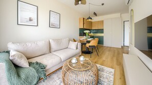 A modern living room with a sofa, a coffee table, and a dining area with chairs. - Apartamenty Sun & Snow The One Ustronie Morskie (Sianożęty)