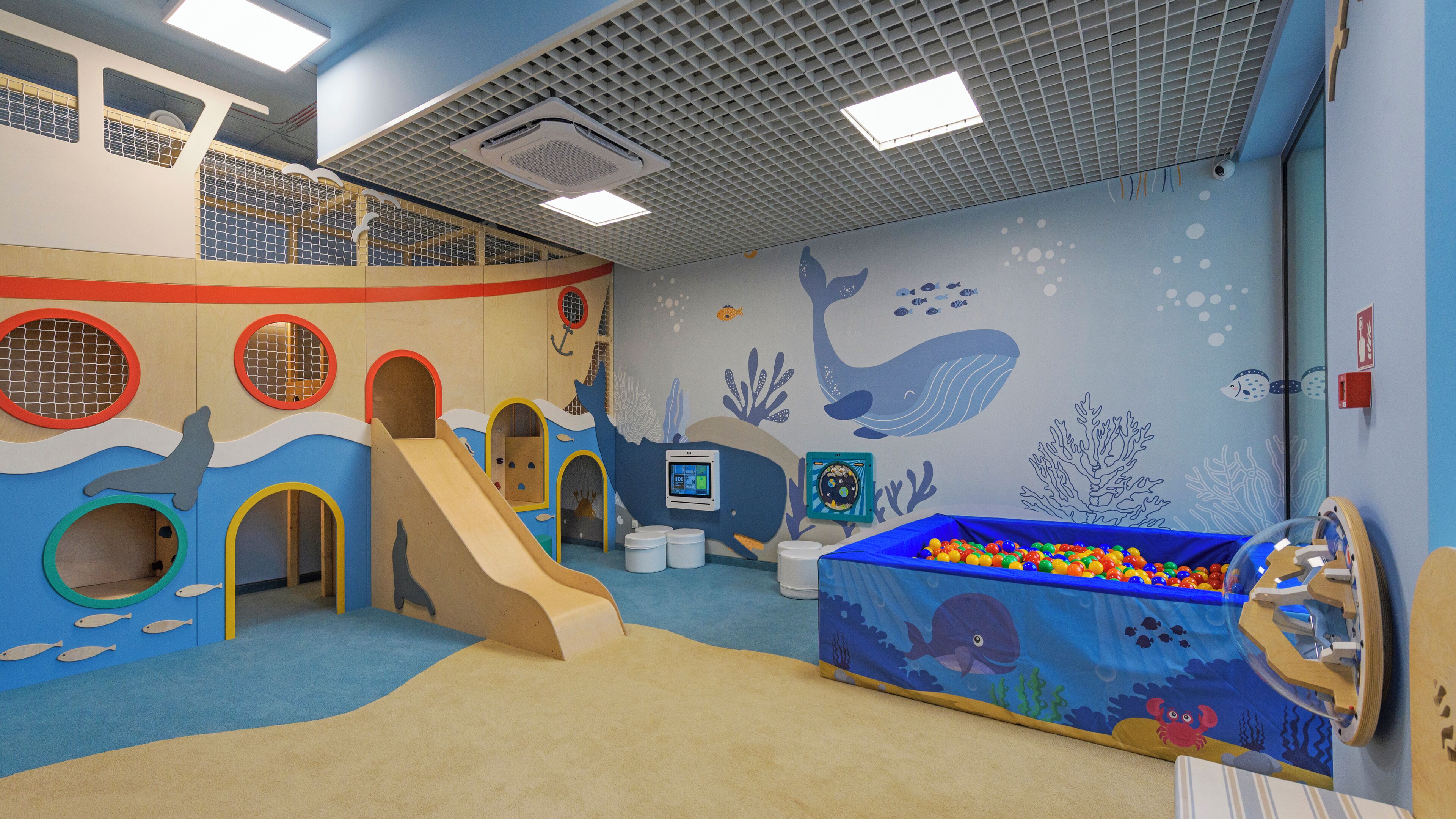 Ein Kinderspielbereich mit Rutsche, Bällebad und Wandmalereien von Meeresbewohnern.