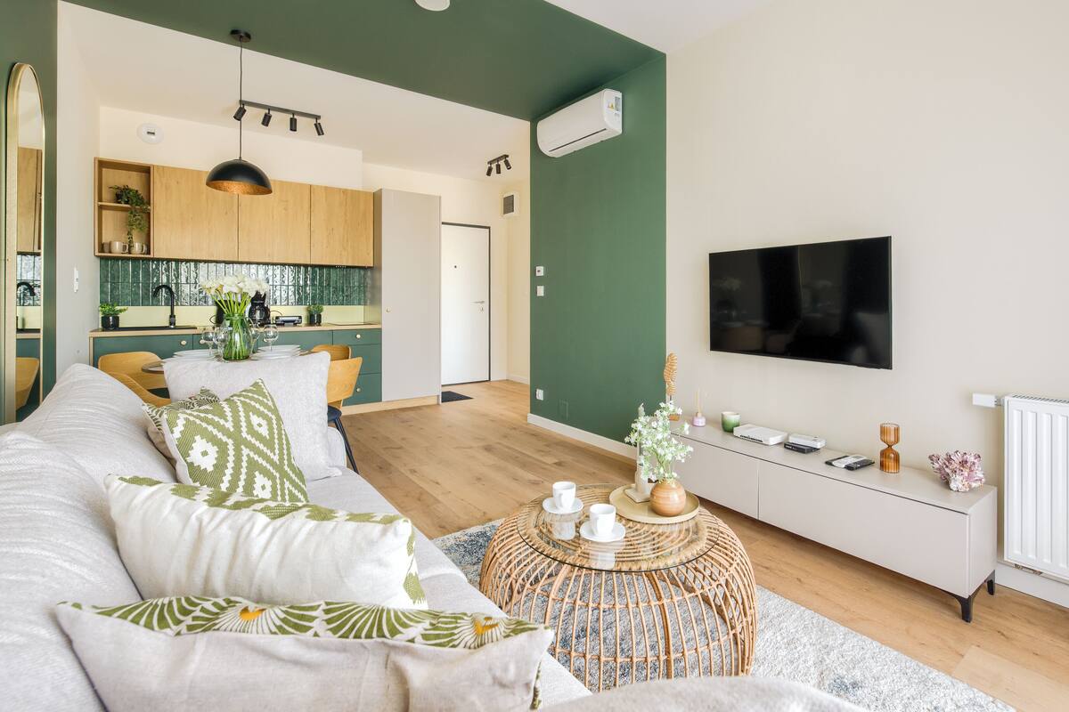 Ein modernes Wohnzimmer mit einer Couch, einem runden Couchtisch, einem Fernseher und einer Küche im Hintergrund.
