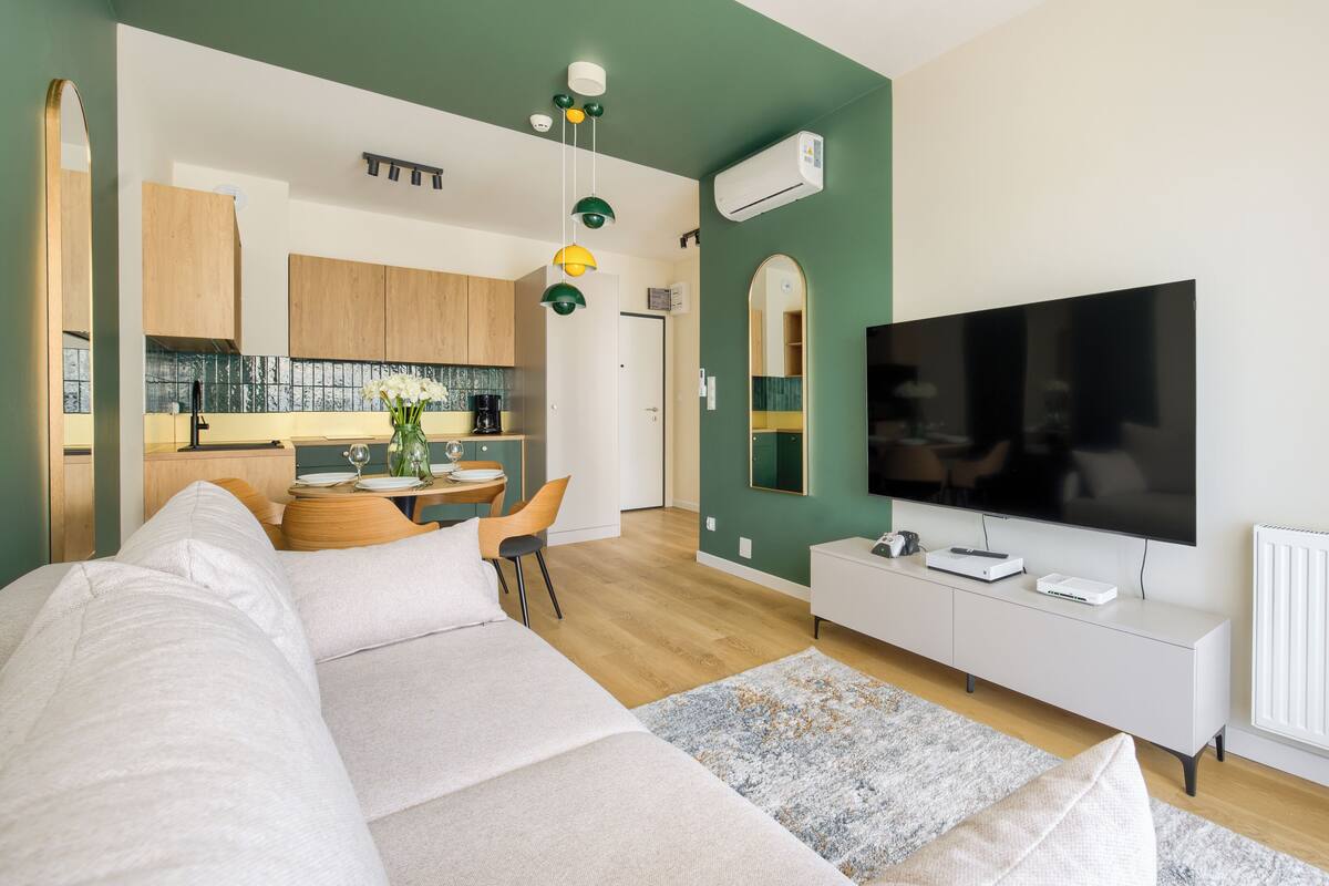Ein modernes Wohnzimmer mit einer Couch, einem Fernseher und einem Essbereich mit Tisch und Stühlen.