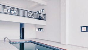Une piscine intérieure moderne, avec une eau d’un bleu limpide, une rambarde en métal noir et une bordure carrelée.