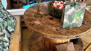 Ein runder Holztisch mit rustikaler Optik, umgeben von Holzbanken mit tropischen Blattmustern.