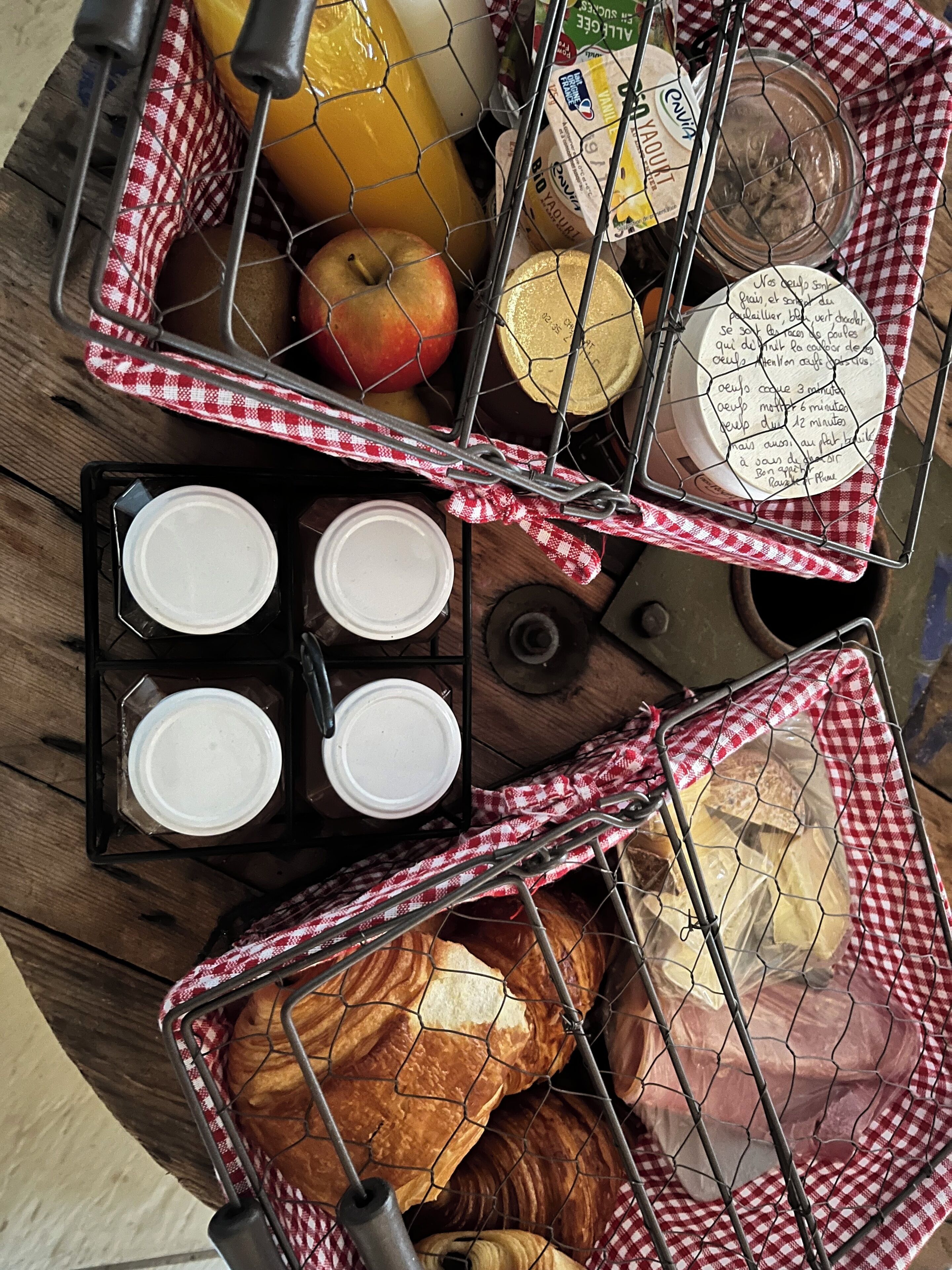 A wooden table with baskets containing bread, apples, cheese, and jars.