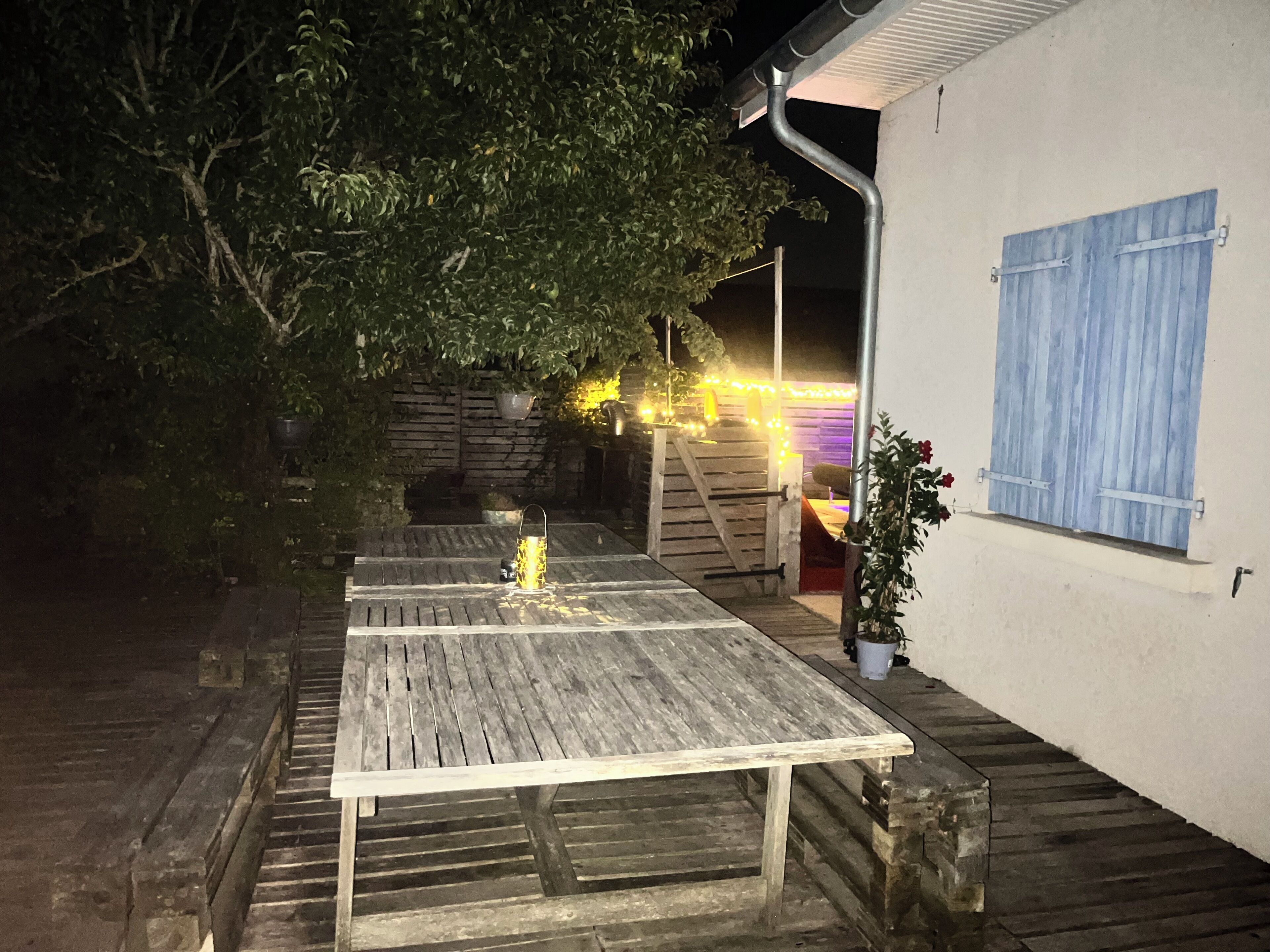 Une table en bois à utiliser en extérieur, dotée d’un cadre en métal et entourée d’une terrasse en bois.