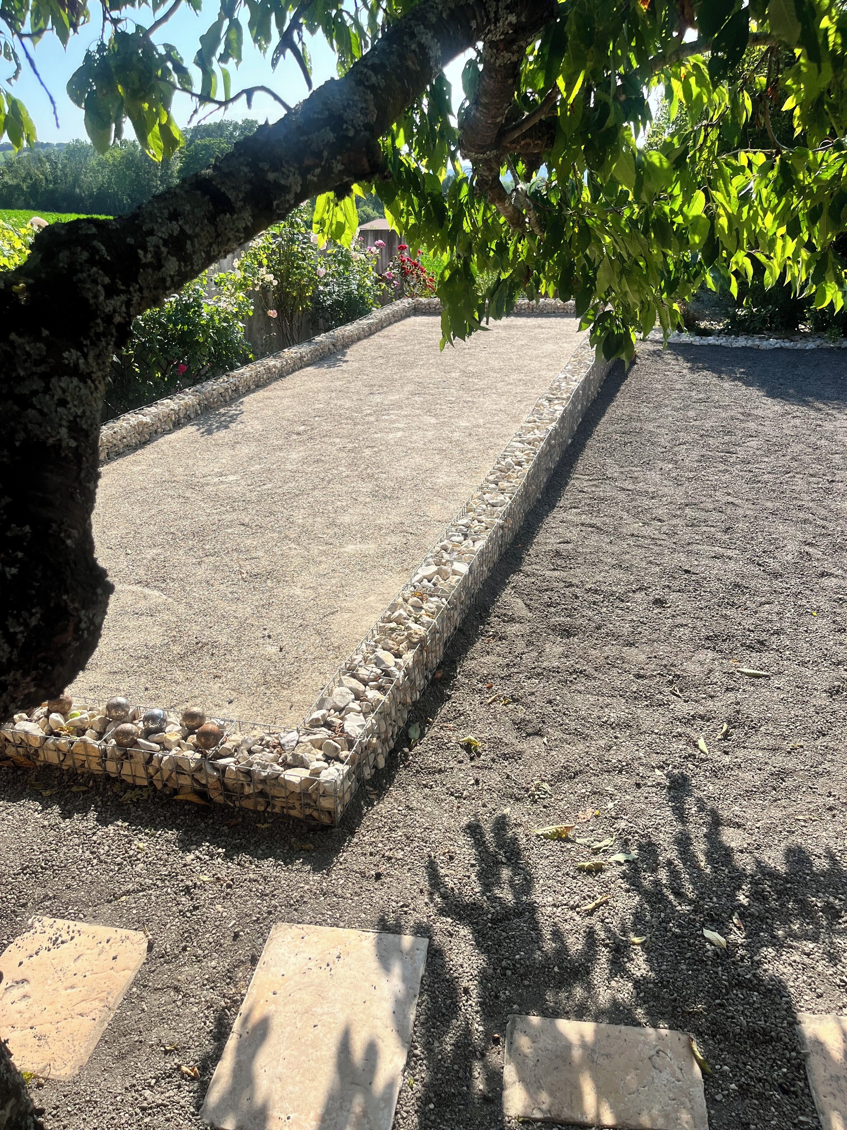 A paved area with a stone border, surrounded by greenery and a tree.