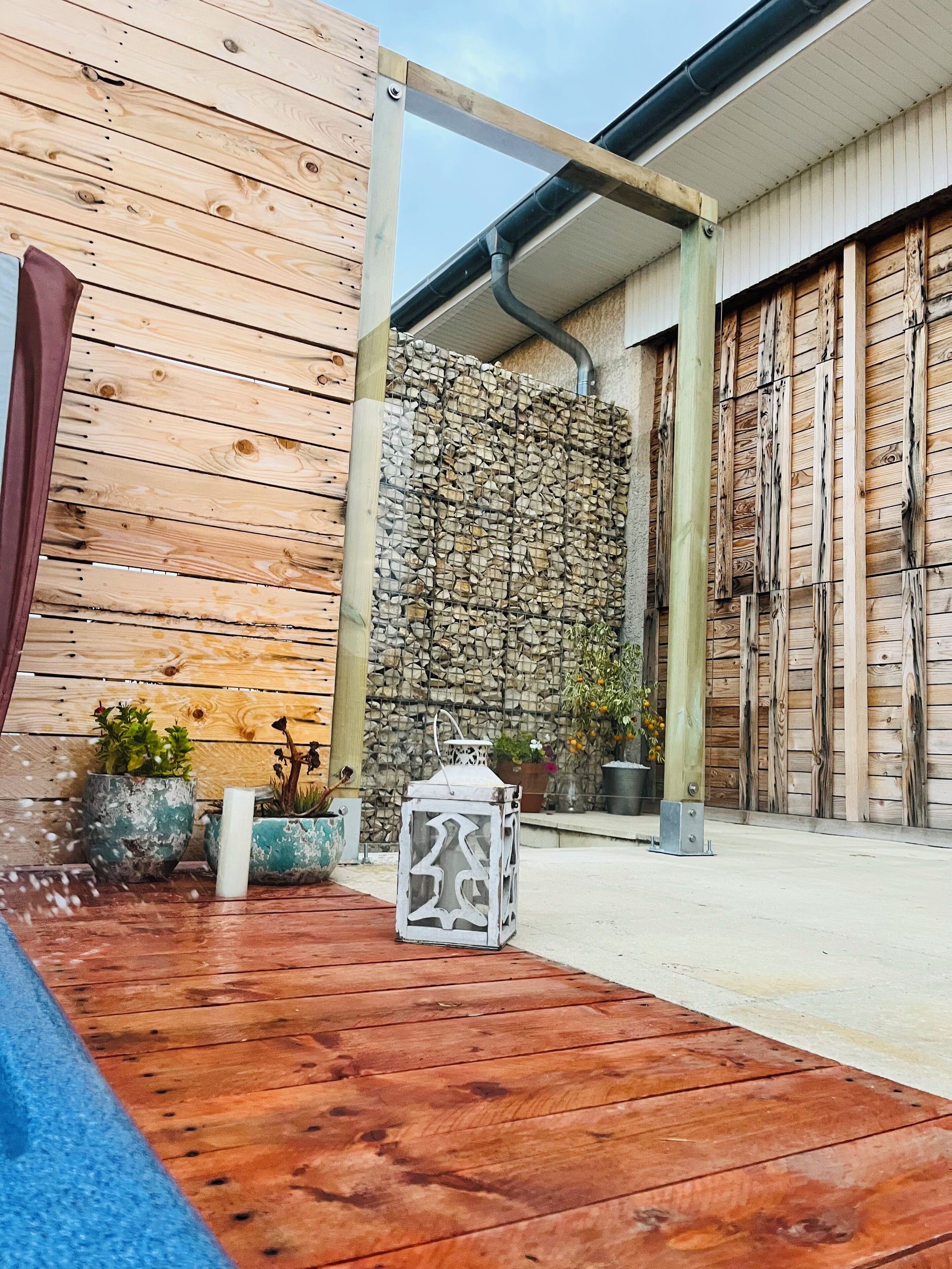 Une terrasse en bois avec un muret en pierre et des plantes en pot.